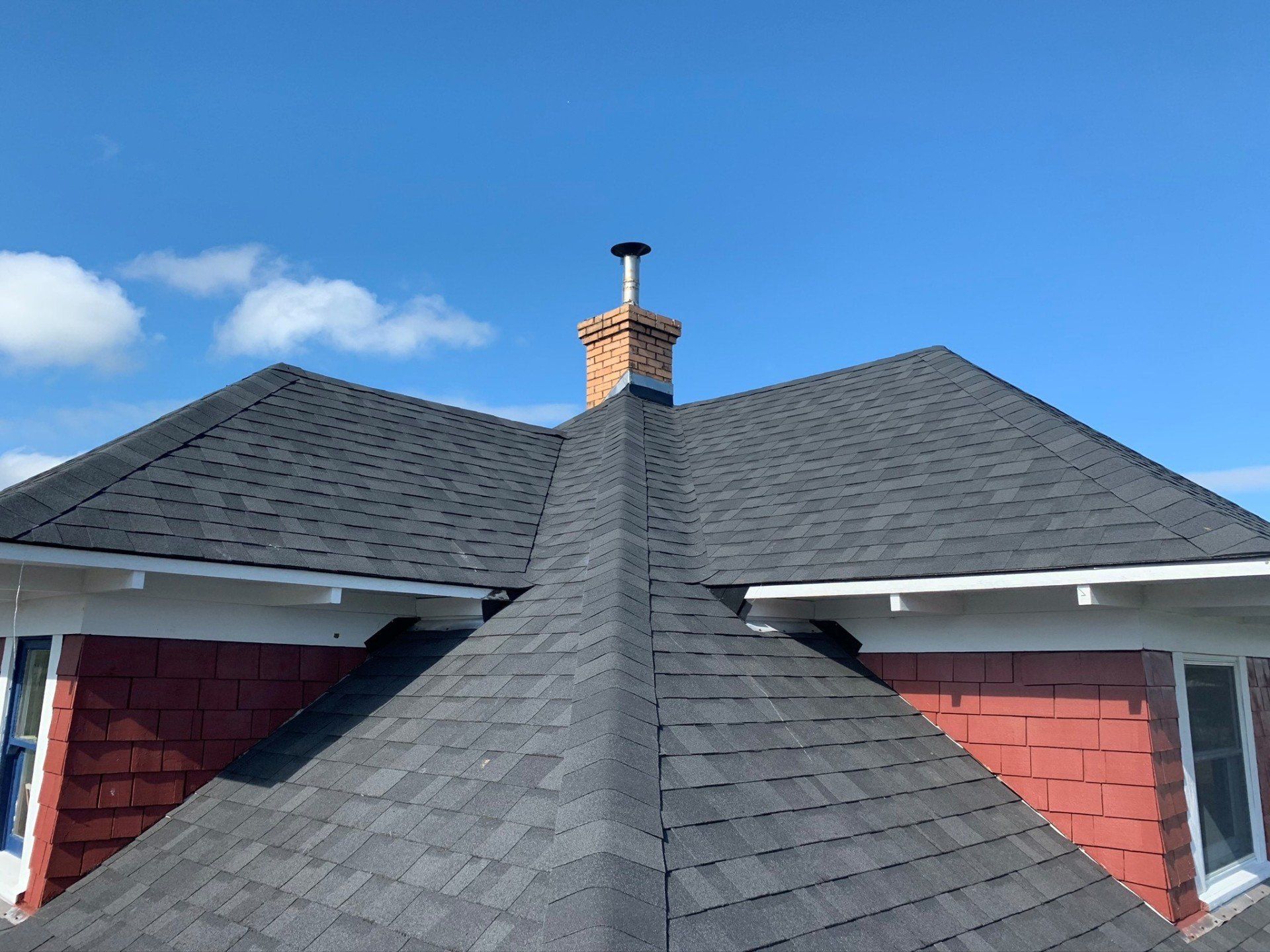 Dark shingle roof with a brick chimney against a blue sky.