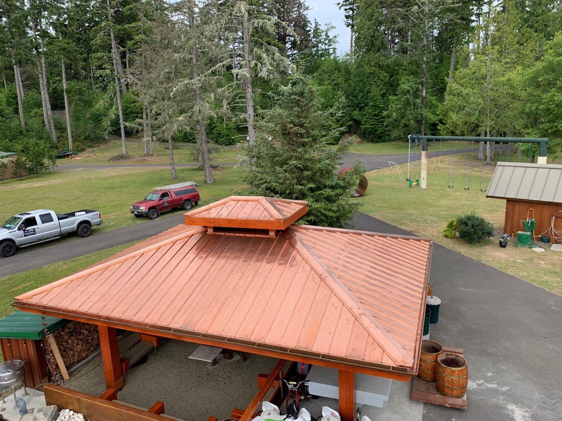 Copper-roofed gazebo with cars on a driveway, surrounded by trees and a grassy yard.