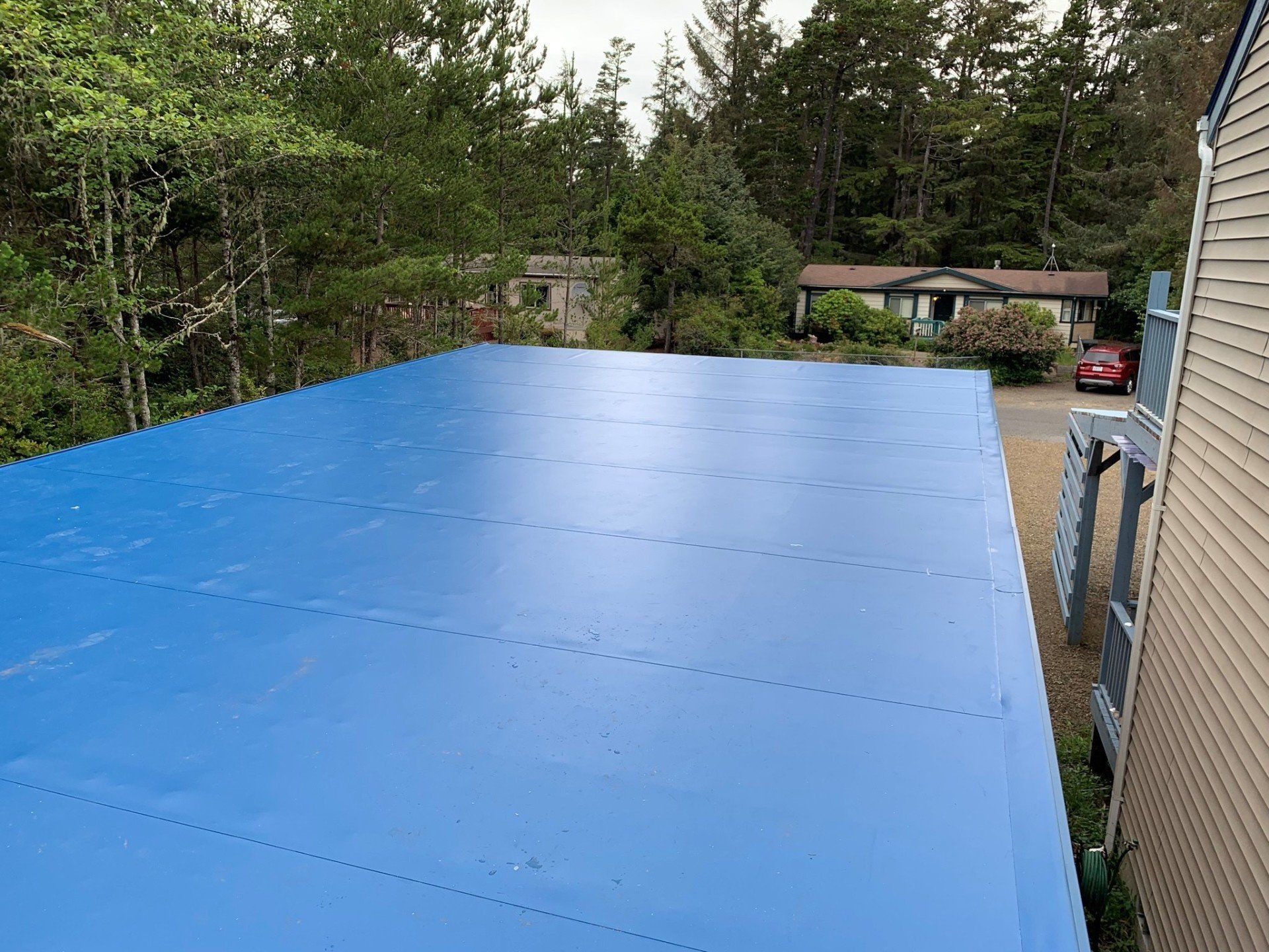 Blue flat roof on a building with trees and other buildings in the background.