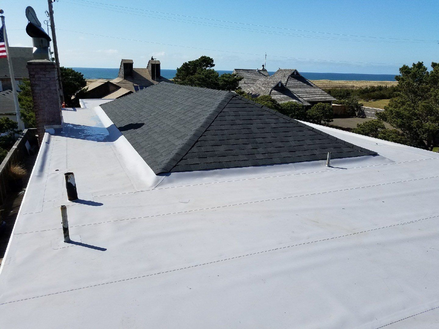Flat white roof with a dark gray shingled section, chimney, and ocean view in the background.