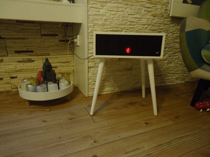 A white speaker is sitting on a wooden table in a living room.