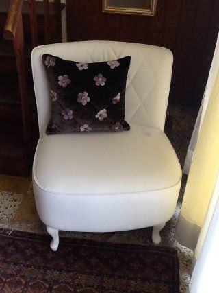 Poltrona imbottita bianca con cuscino floreale nero.