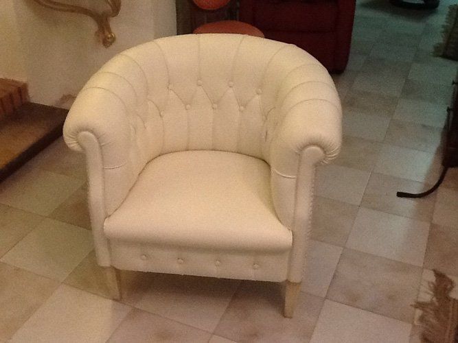 Poltrona color crema con bottoni trapuntati in una stanza con pavimento piastrellato.