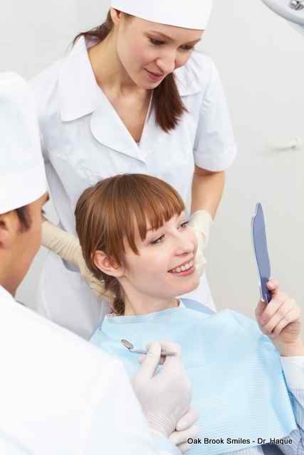 Woman smiles at her teeth in a mirror, dental staff observes in a clinic.