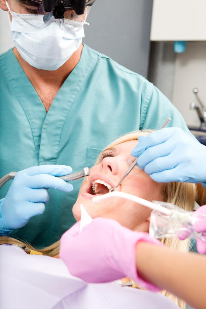 Dentist performing dental work on patient with assistant; dental office setting.