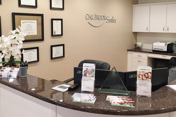 Reception desk at Oak Brook Smiles dental office, diplomas, brochures, and computer monitors visible.