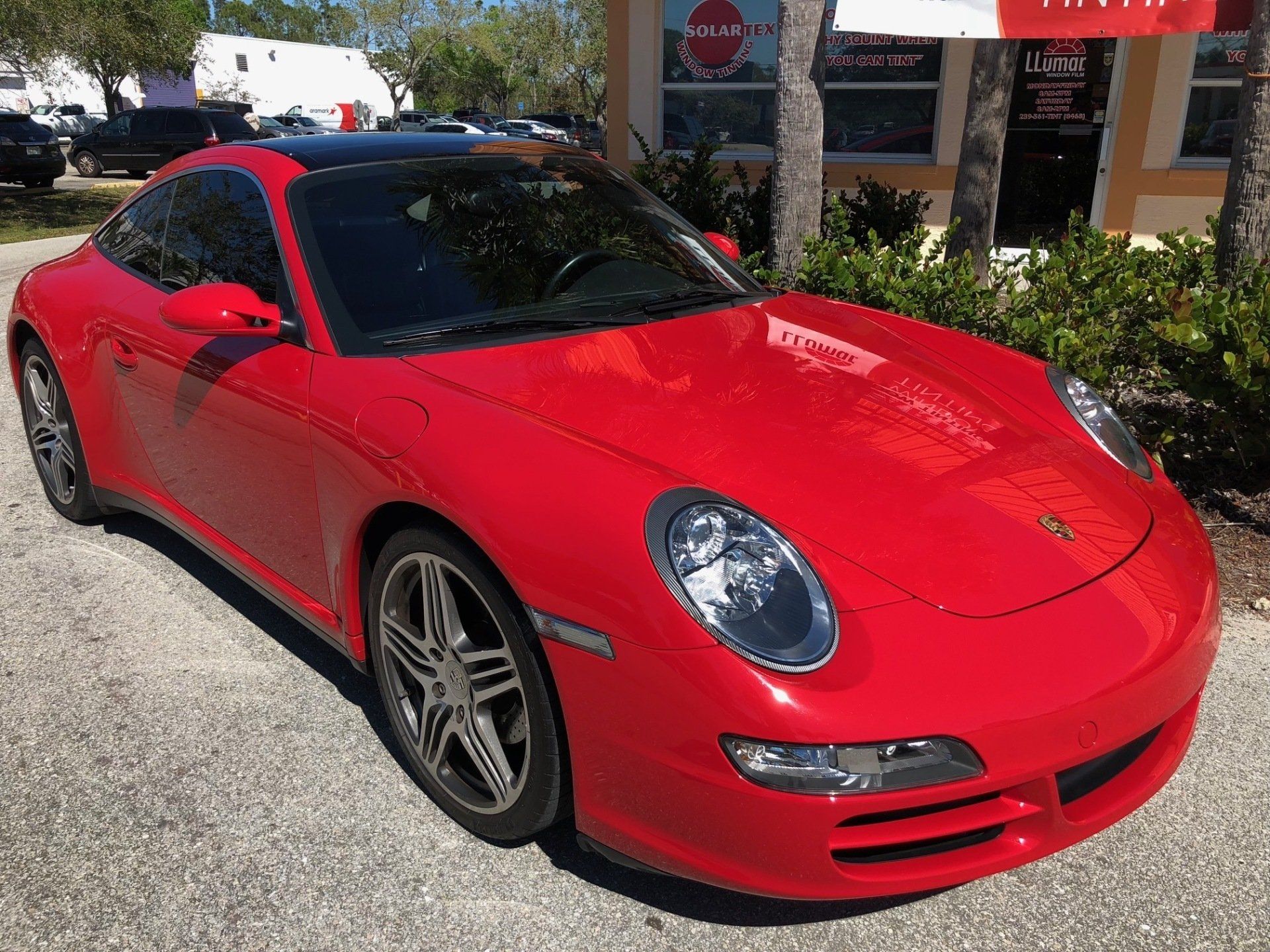 Red Porsche 911 coupe parked on a sunny street.