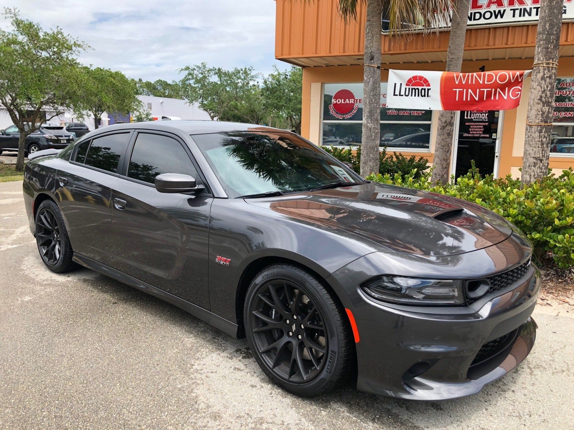 Gray Dodge Charger with tinted windows parked outside a window tinting business.