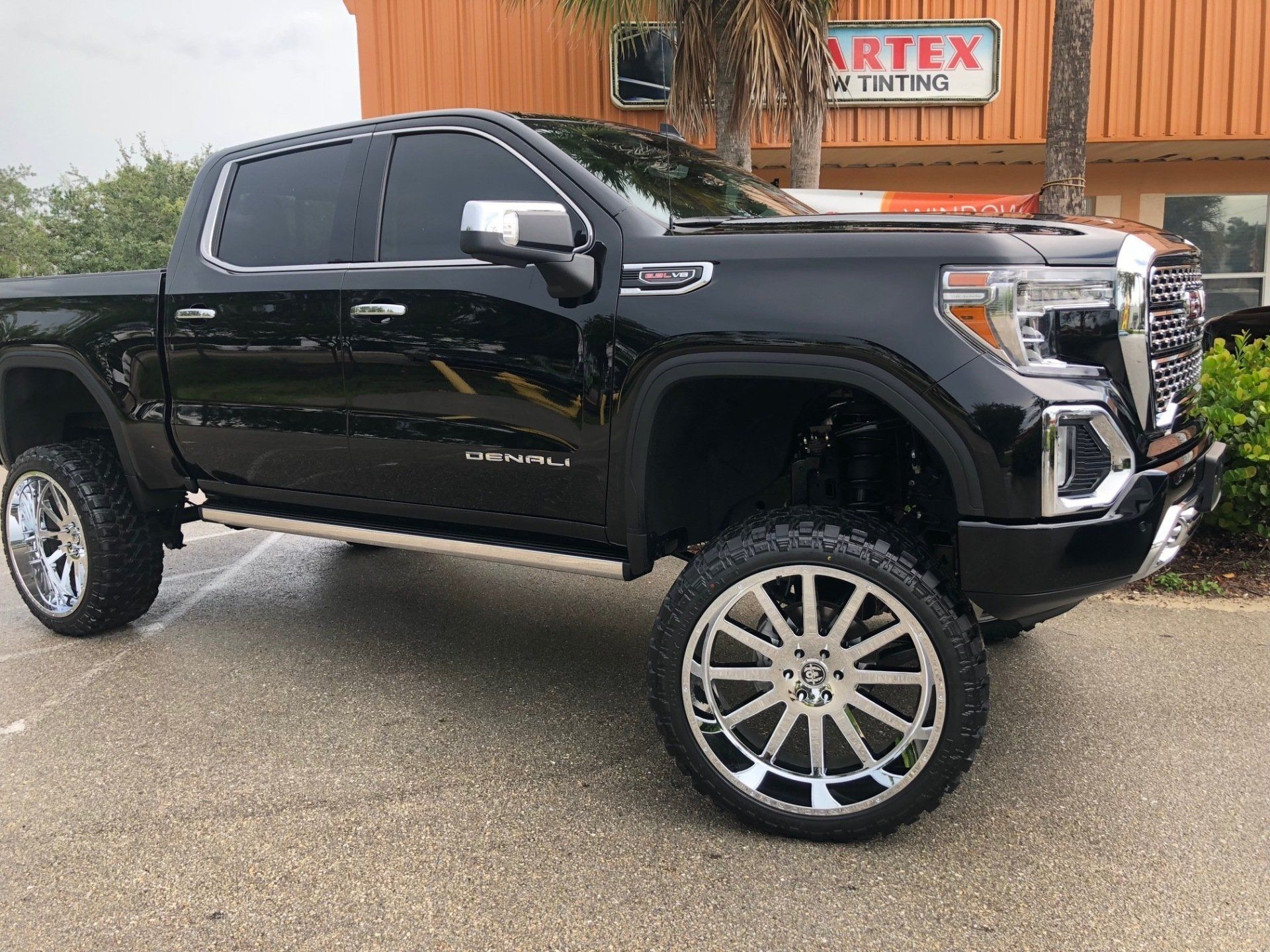 Black lifted GMC truck with chrome wheels parked in front of a building with ARTex Tinting sign.