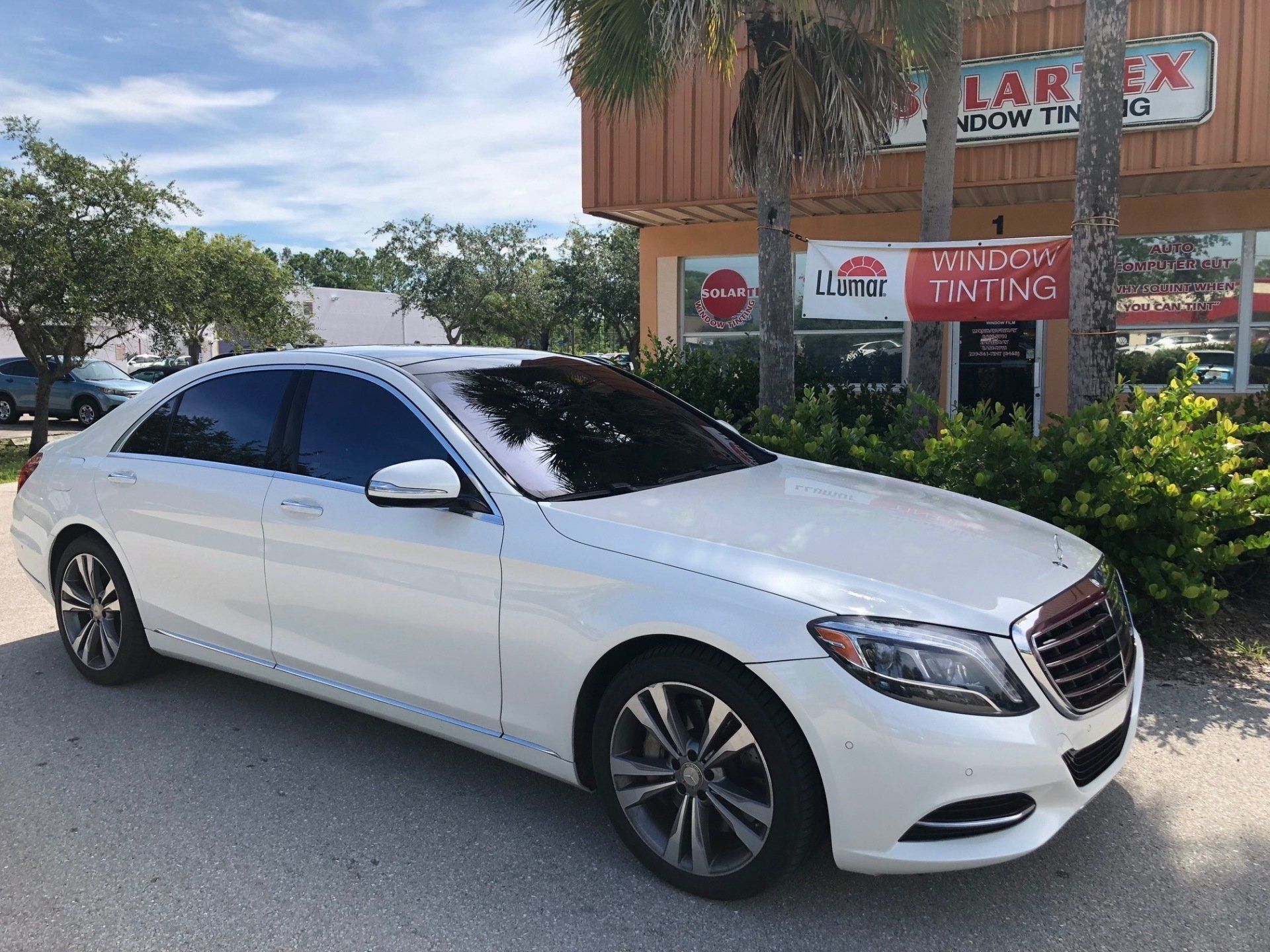 White Mercedes-Benz sedan with tinted windows parked outside a window tinting business on a sunny day.