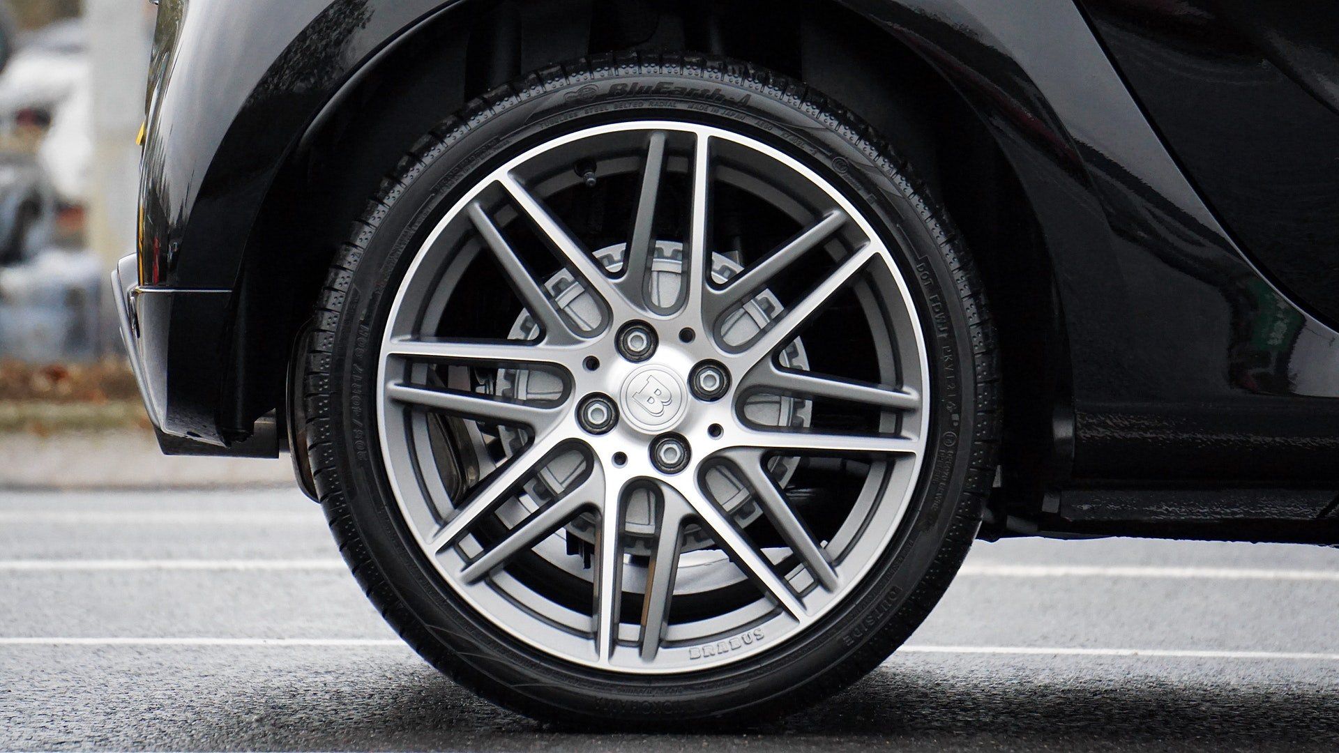 Black car wheel, silver rim, on wet asphalt.