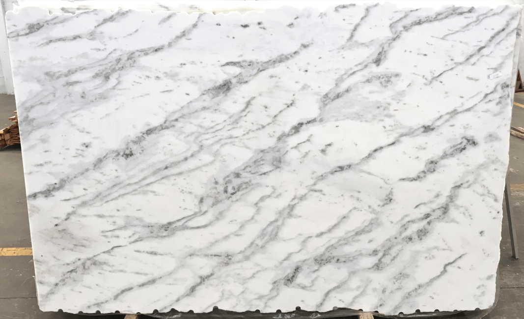 A slab of white marble featuring prominent, diagonal grey veining and subtle dark mineral flecks throughout.