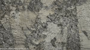 A close-up view of polished granite stone featuring a mottled pattern of white, gray, and dark charcoal veins.