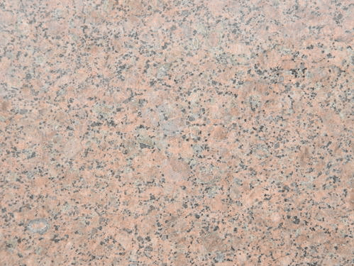 A close-up view of polished pink granite stone with speckled black and grey mineral flecks throughout.