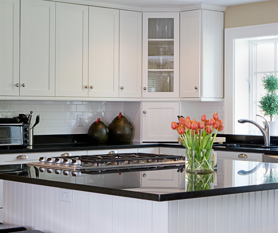 A bright kitchen featuring white cabinets, black countertops, a central island with a gas cooktop, and orange tulips.