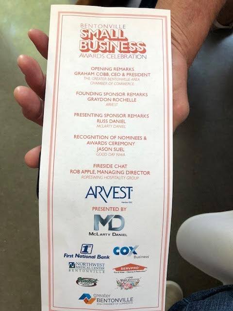 Hand holding a Bentonville Small Business Awards celebration program. It lists sponsors and event details.