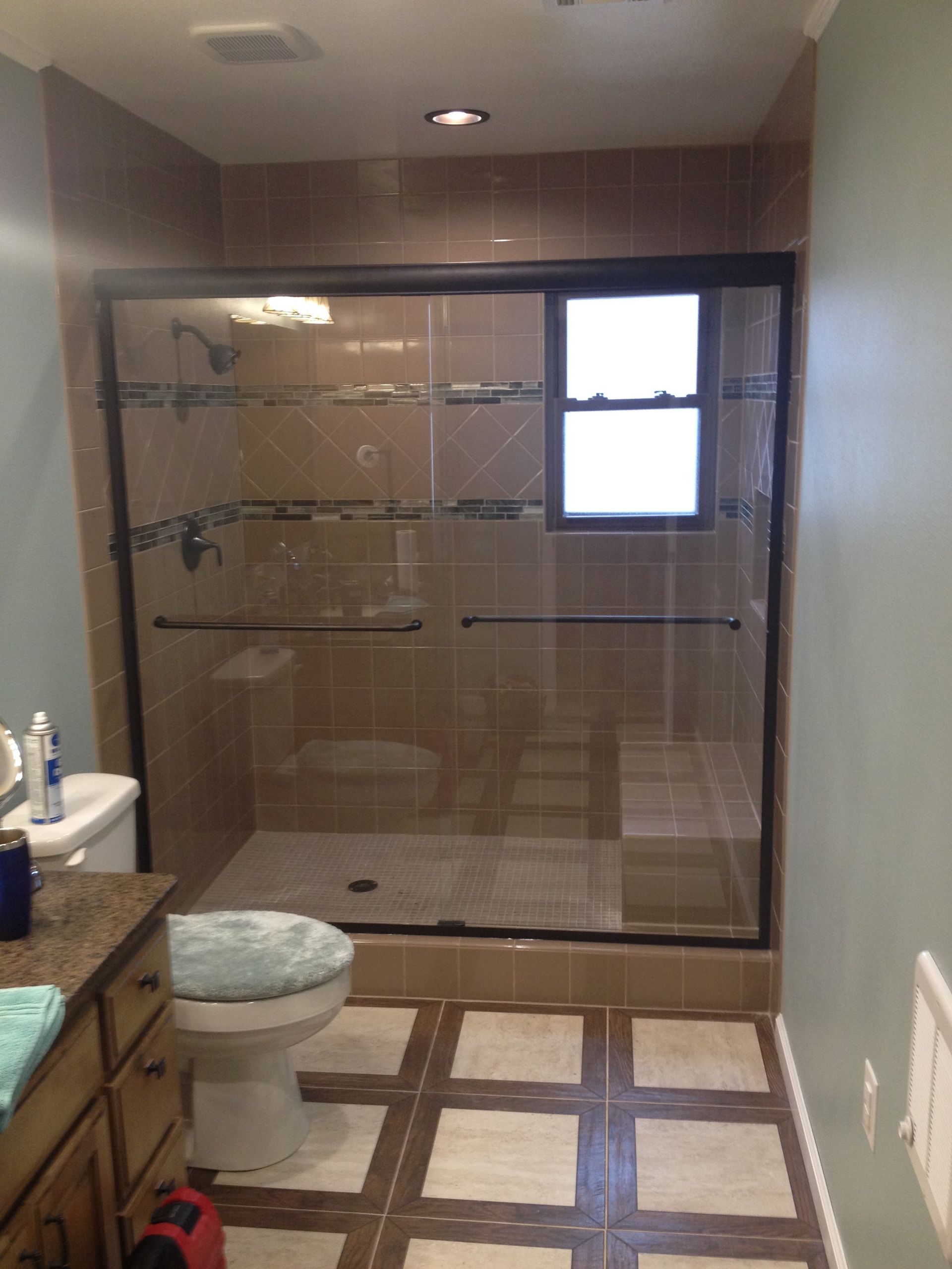 Bathroom with glass shower, toilet, vanity, and window. Brown tile floors, tan shower walls, and blue walls.