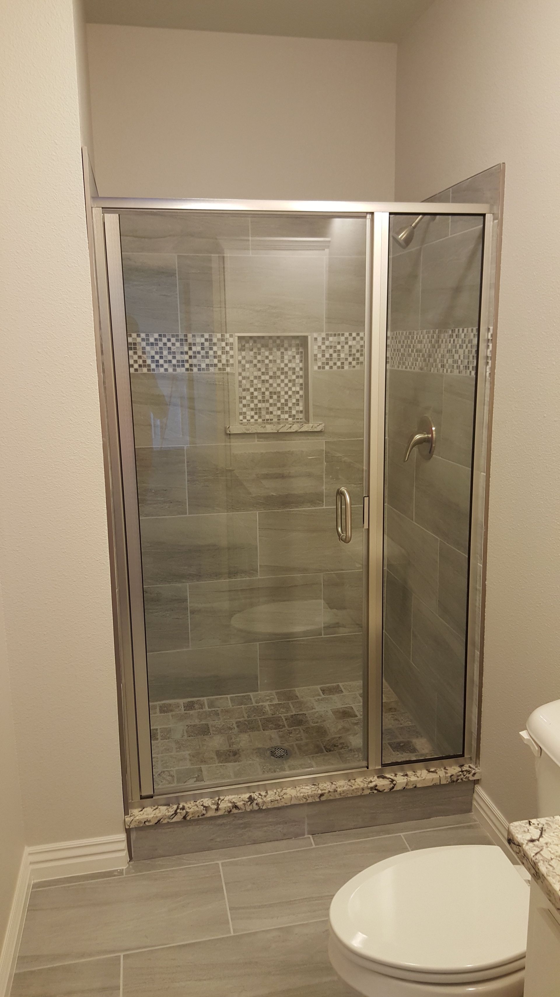 Shower with glass door, stone tile, and mosaic accent in a bathroom.