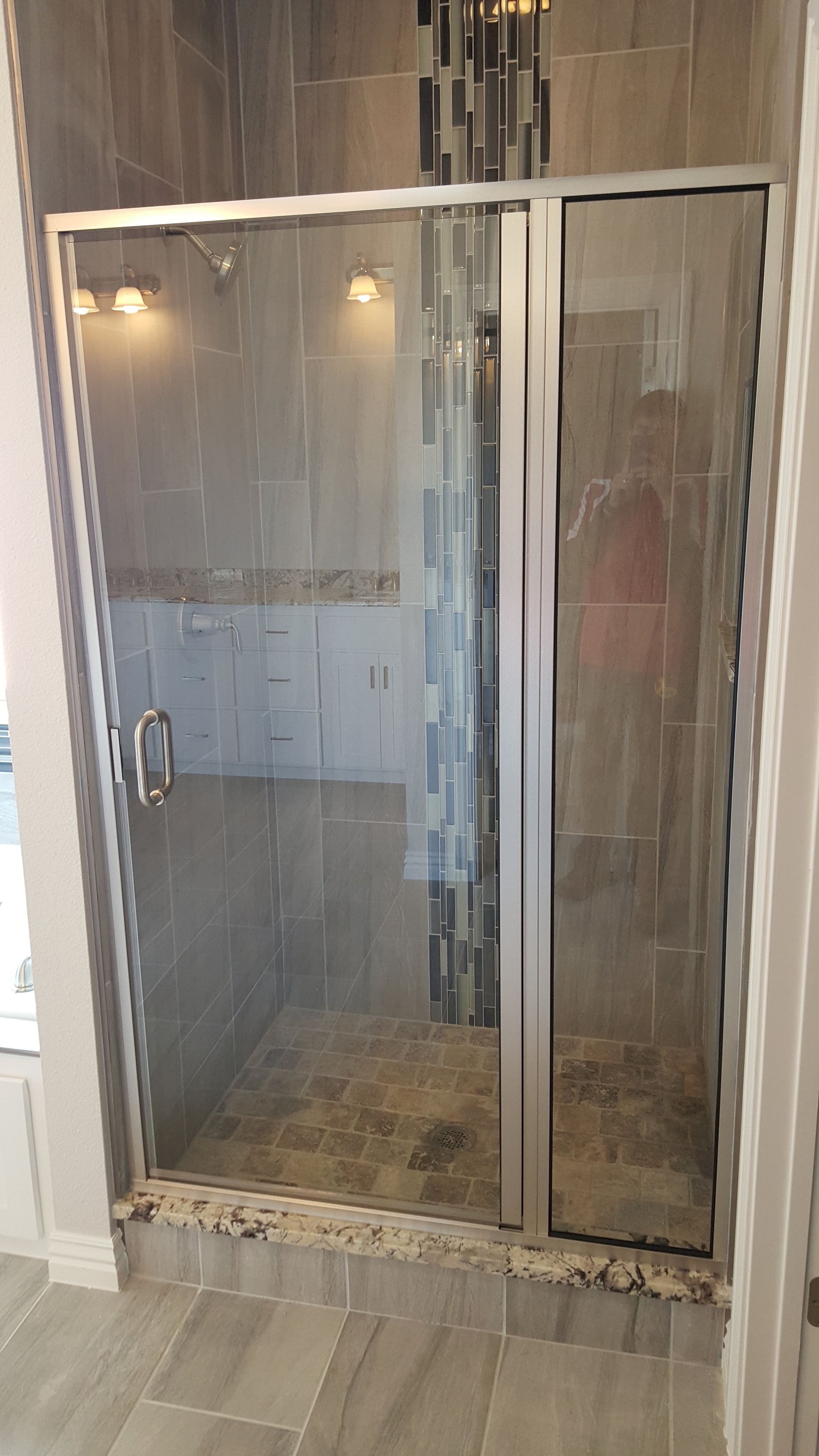 Glass shower enclosure with gray tile, stone floor, and mosaic accent.