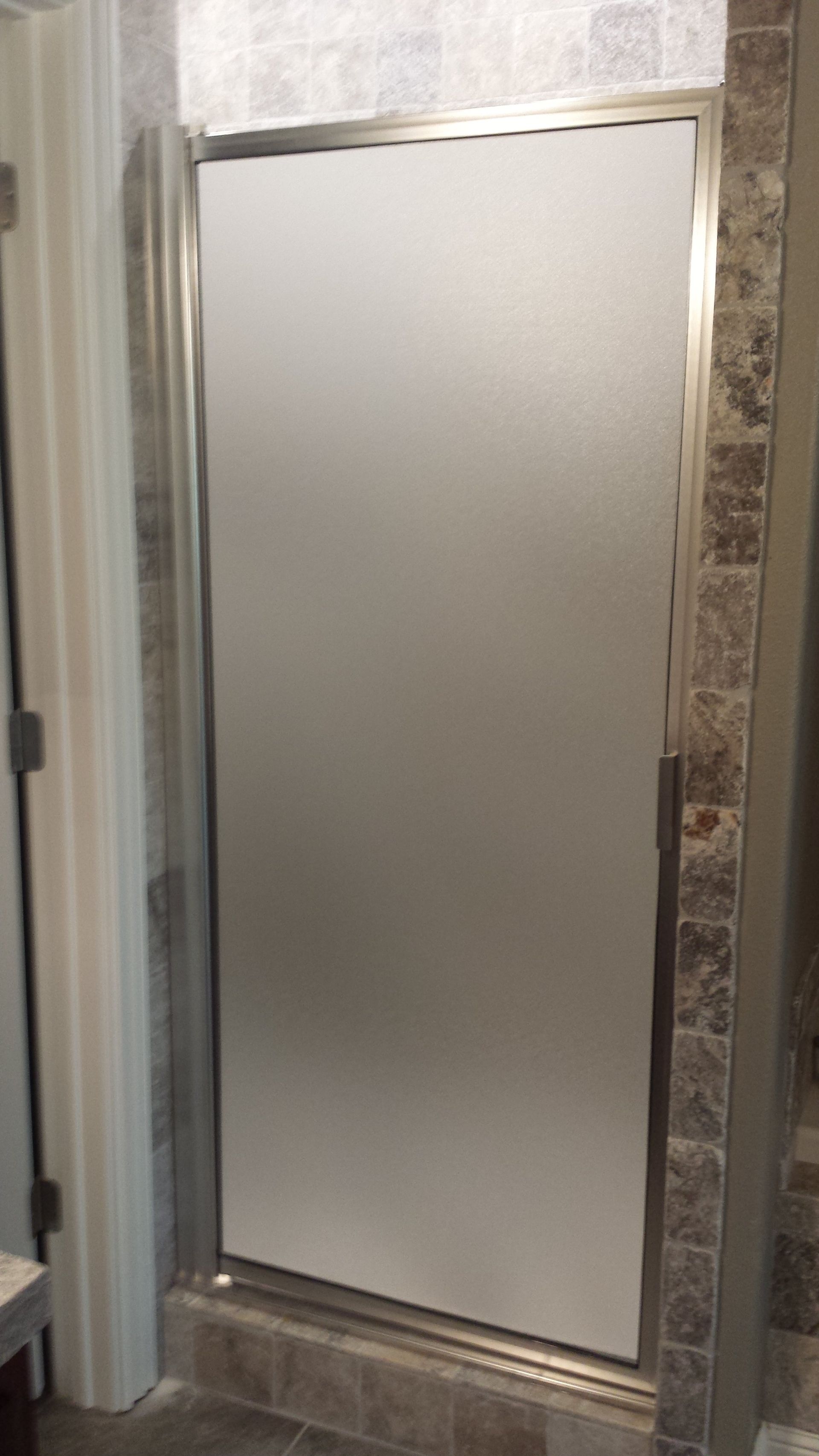 Frosted glass shower door with chrome trim, against a tiled wall.