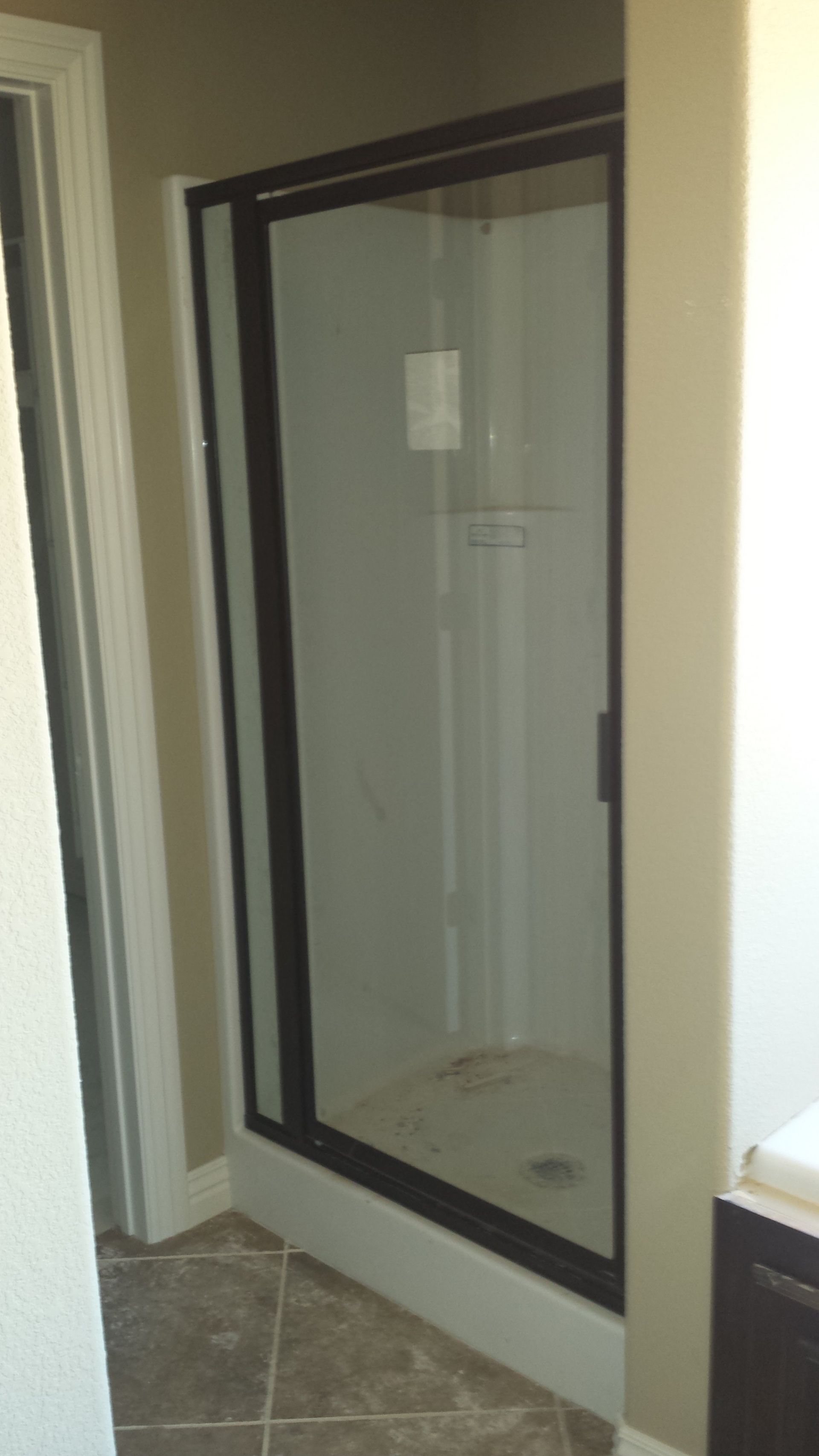 Shower with black frame, glass door, and white interior. Tan walls, tiled floor.