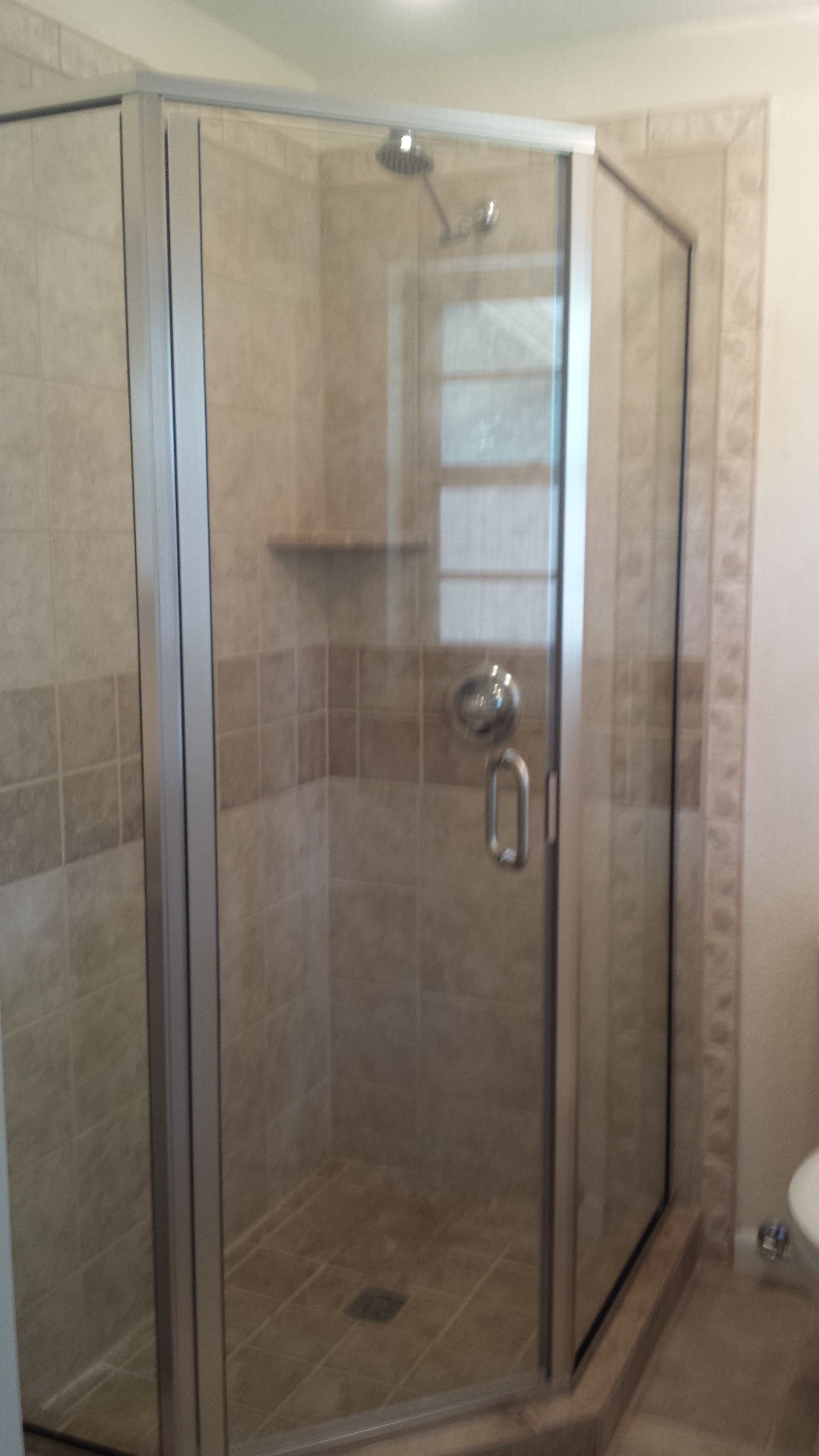 A corner shower with glass doors, tan tile, and chrome fixtures.