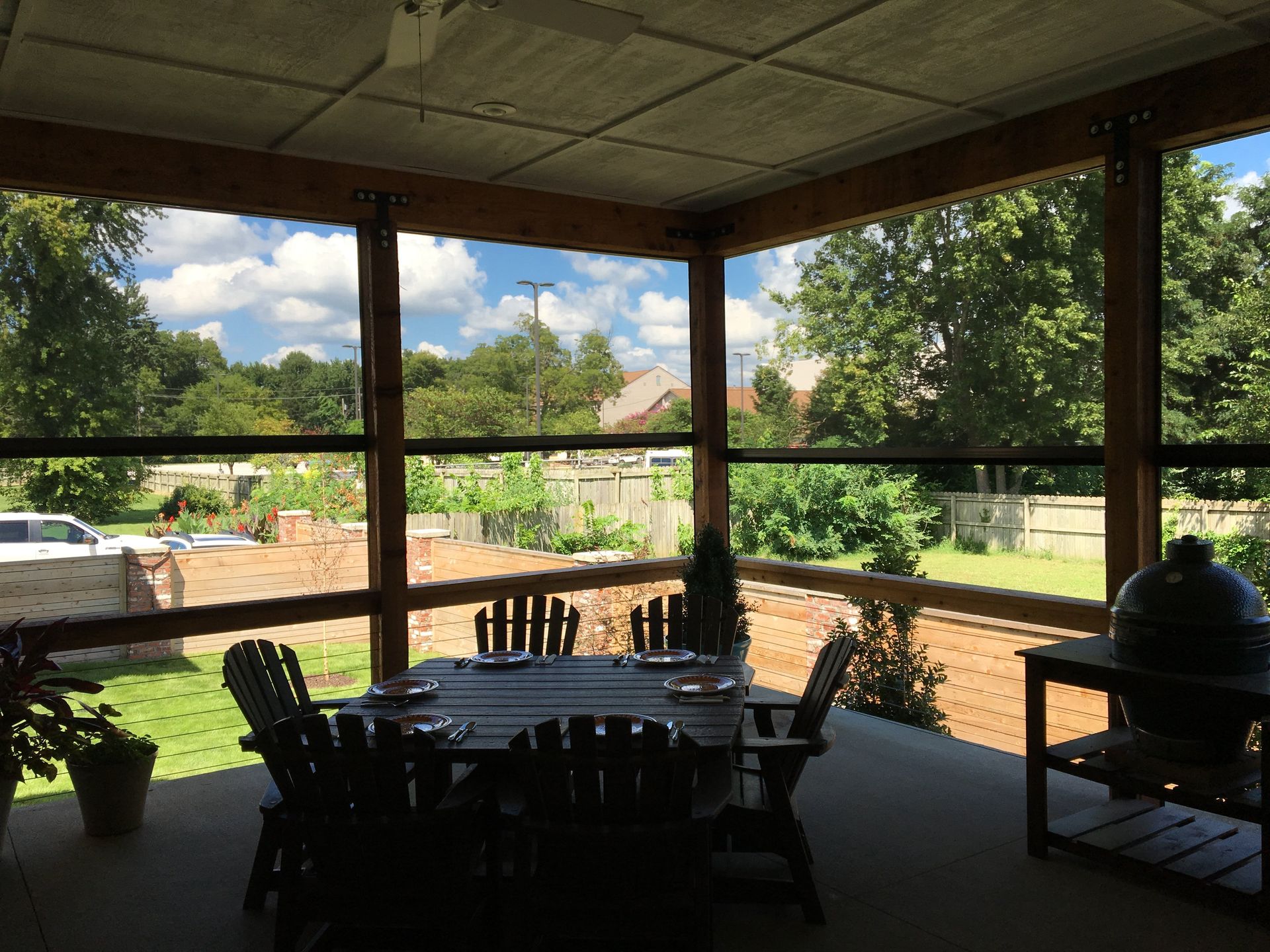 Screened-in porch with a wooden table and chairs. Sunlight streams through screens, showcasing a backyard and blue sky.