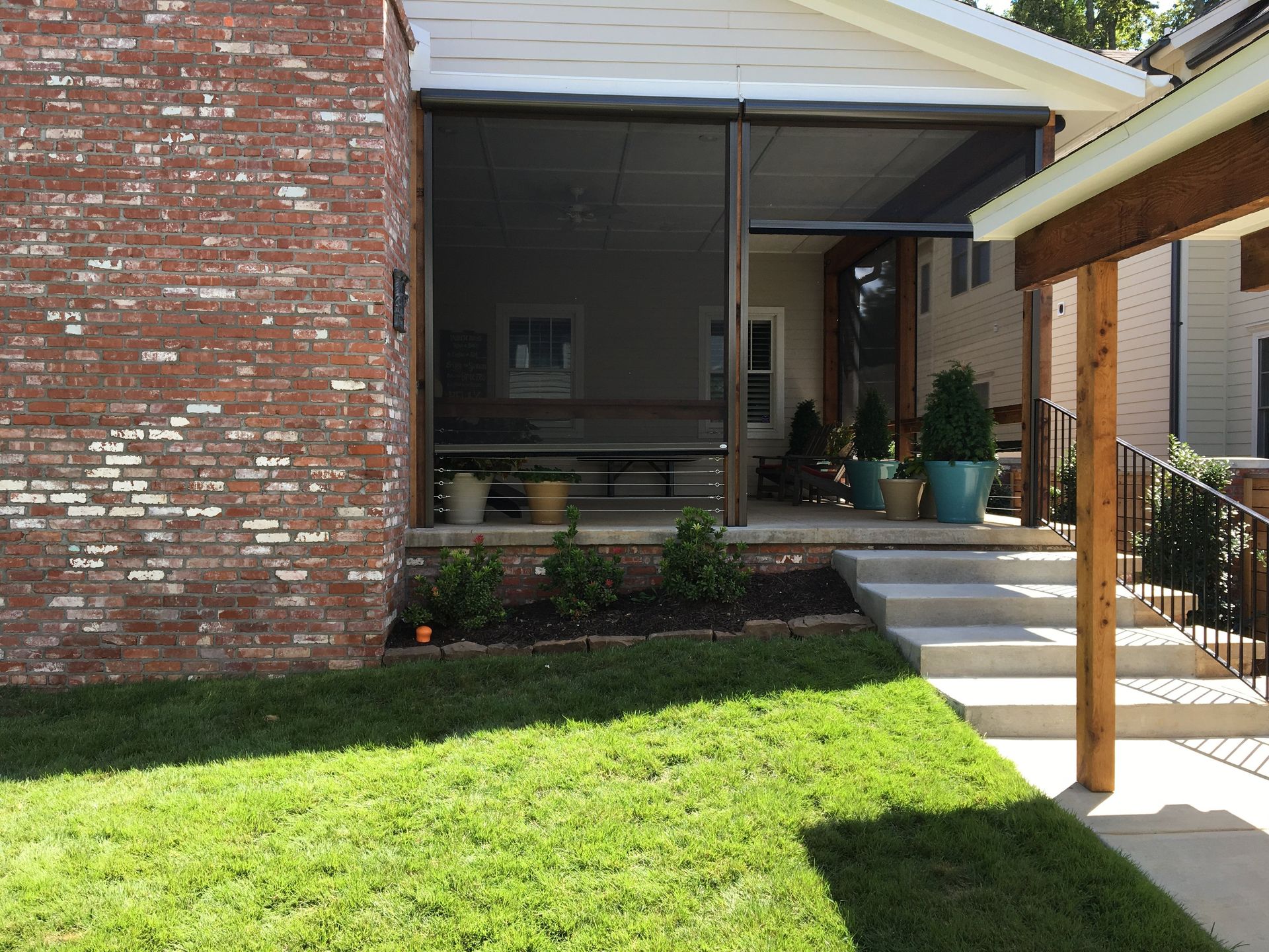A screened porch with red brick, gray steps, and green lawn.