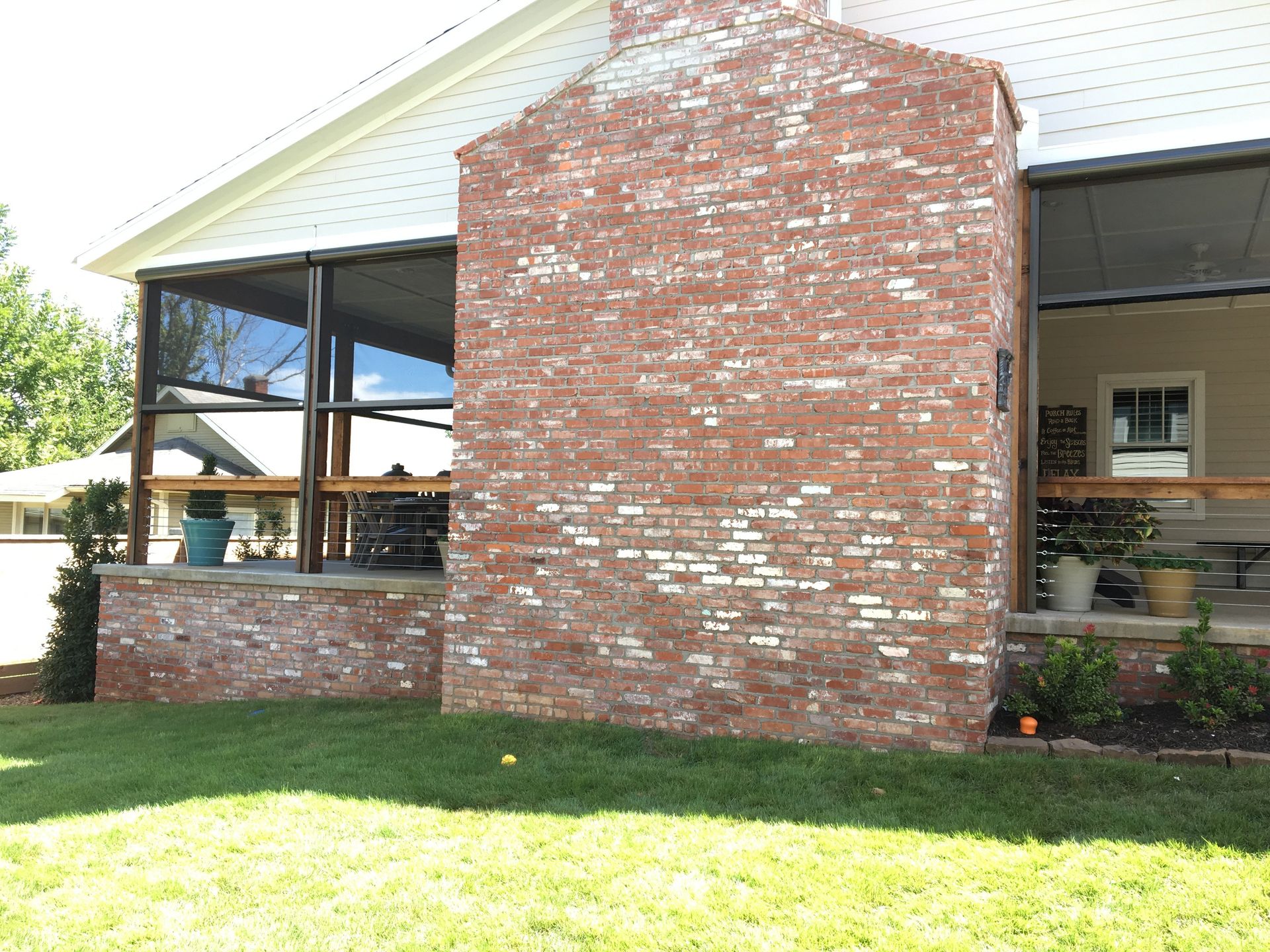 Red brick chimney on a white house with a screened-in porch. Green grass and blue sky.