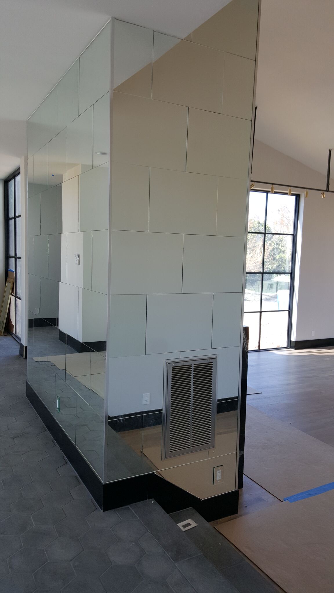 Mirrored wall divider in a light-filled room; black base, HVAC vent, and partially visible windows.