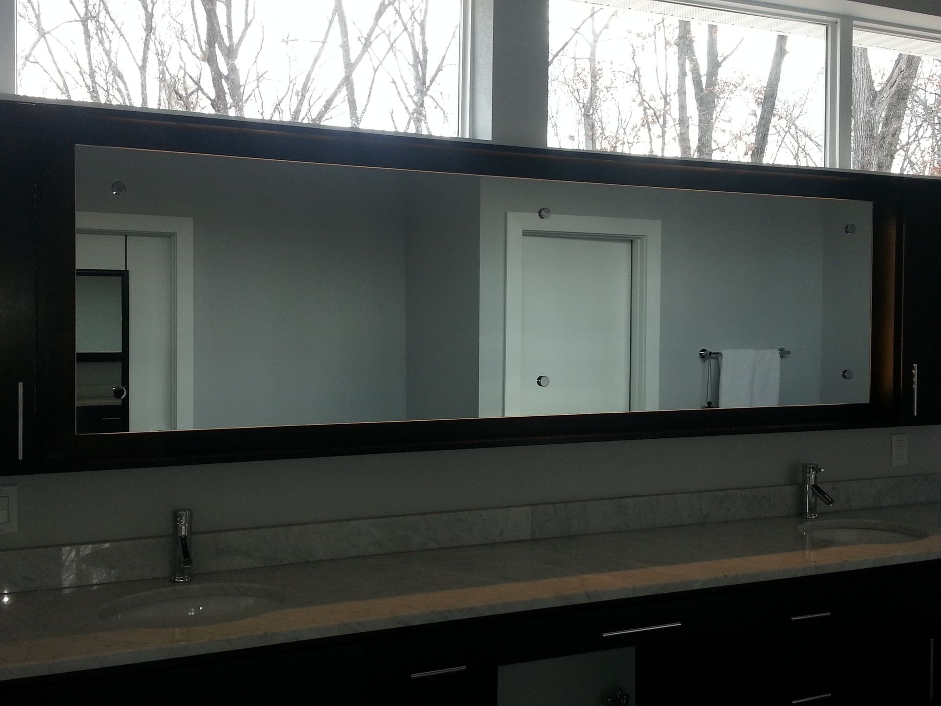 Large mirror above a double sink vanity in a bathroom with a bright window in the background.
