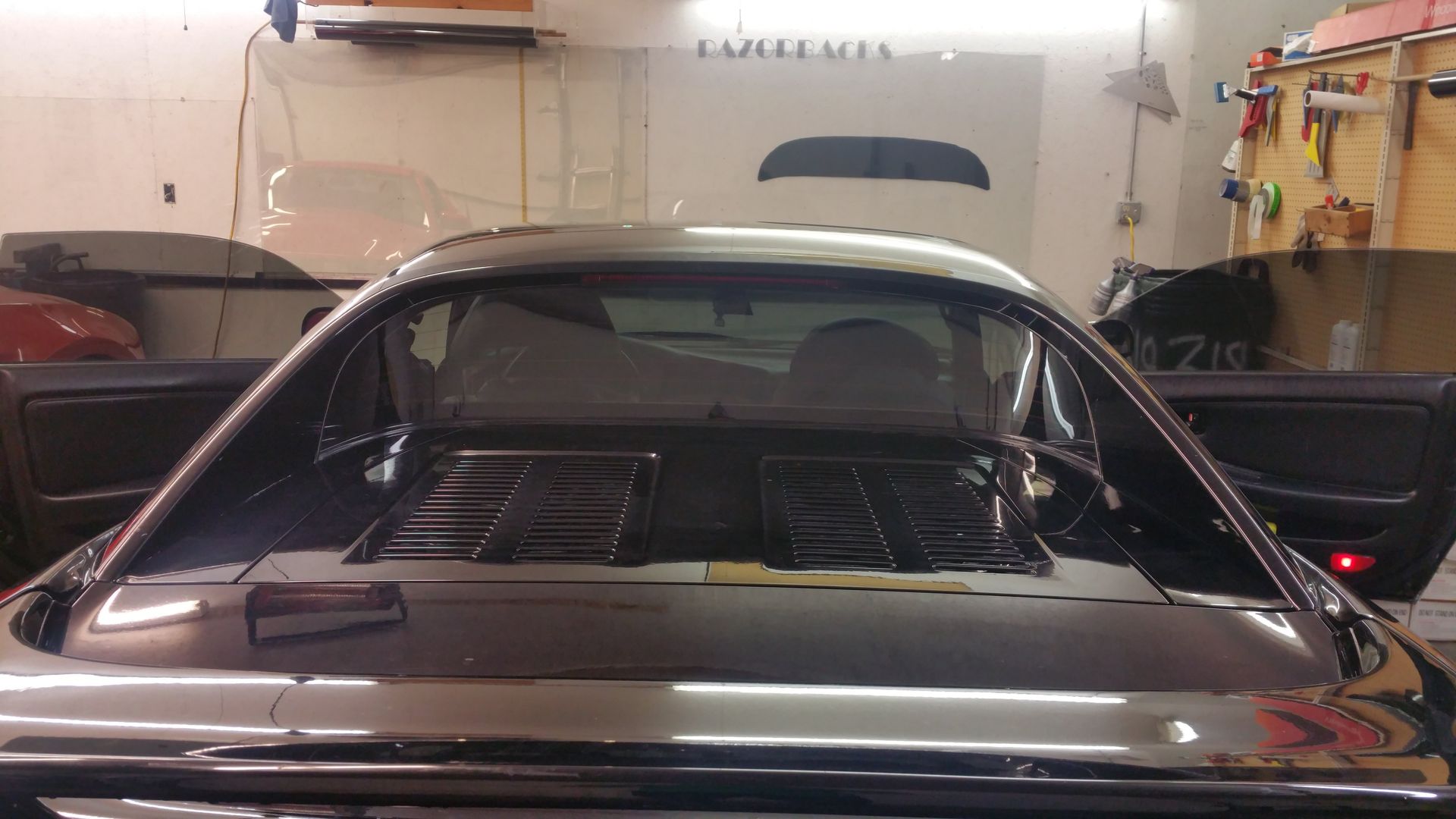 Black sports car with open doors in a garage; rear window and engine bay visible.