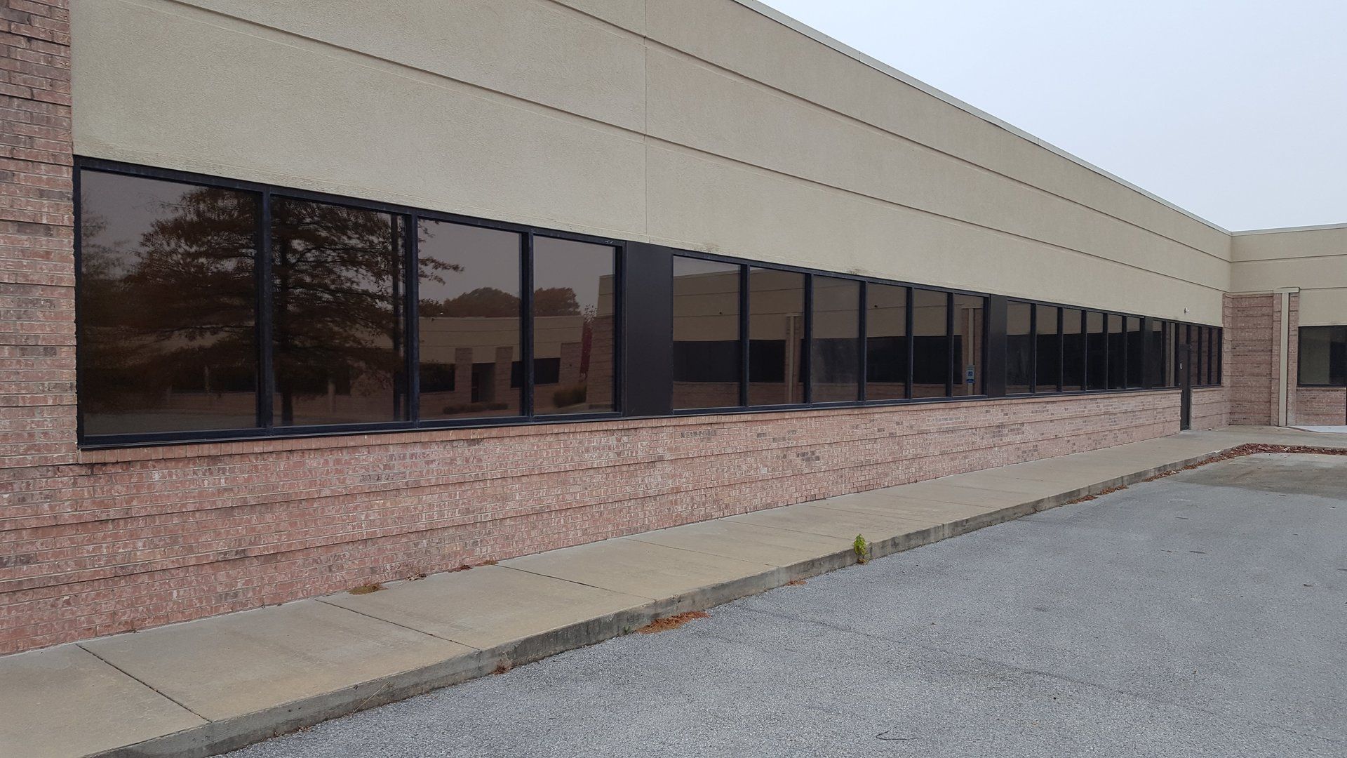 Long, low building with brown-tinted windows, red brick base, and beige upper wall; gray gravel parking lot.