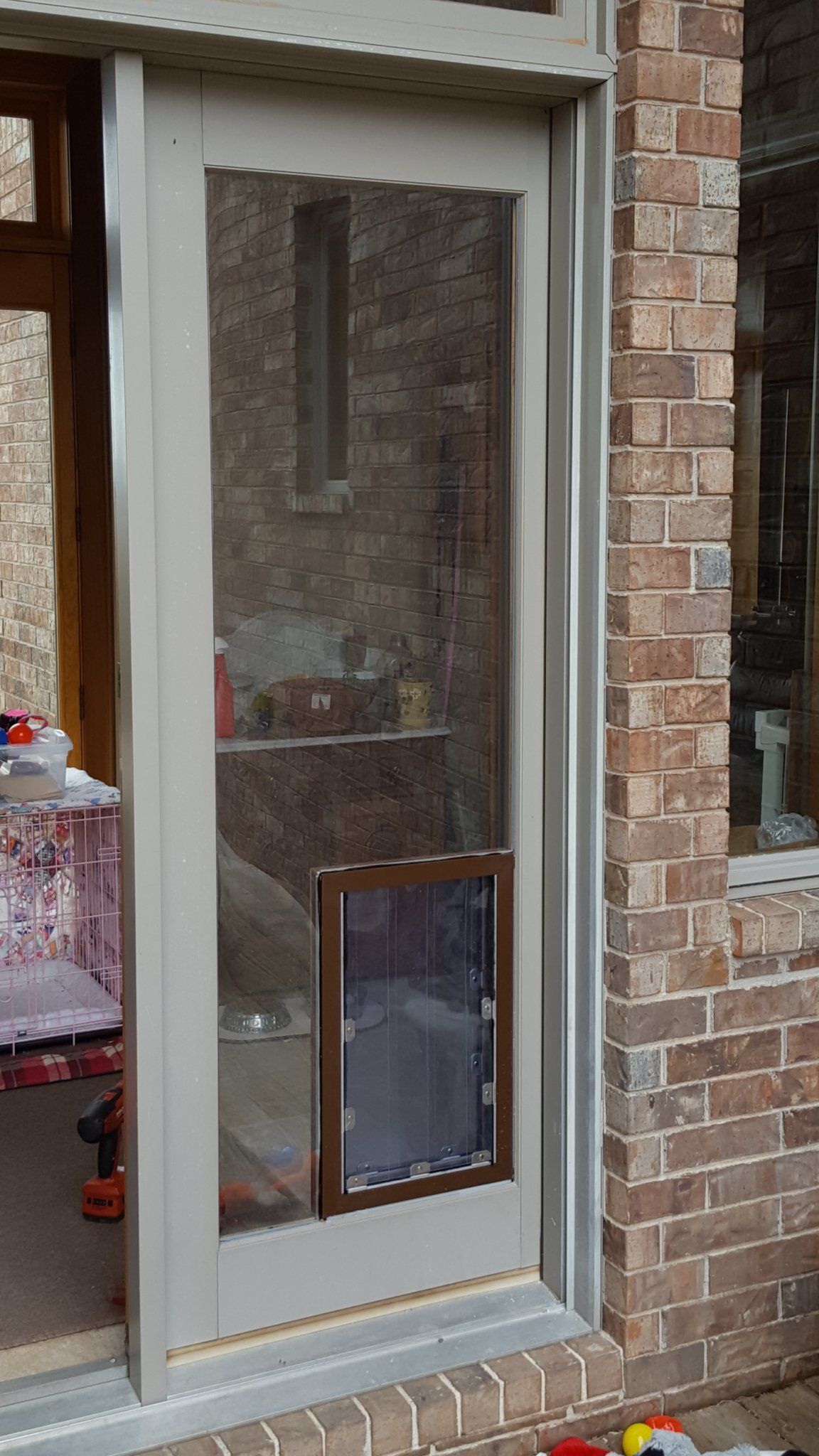 A glass sliding door with a dog door, set in a brick wall.