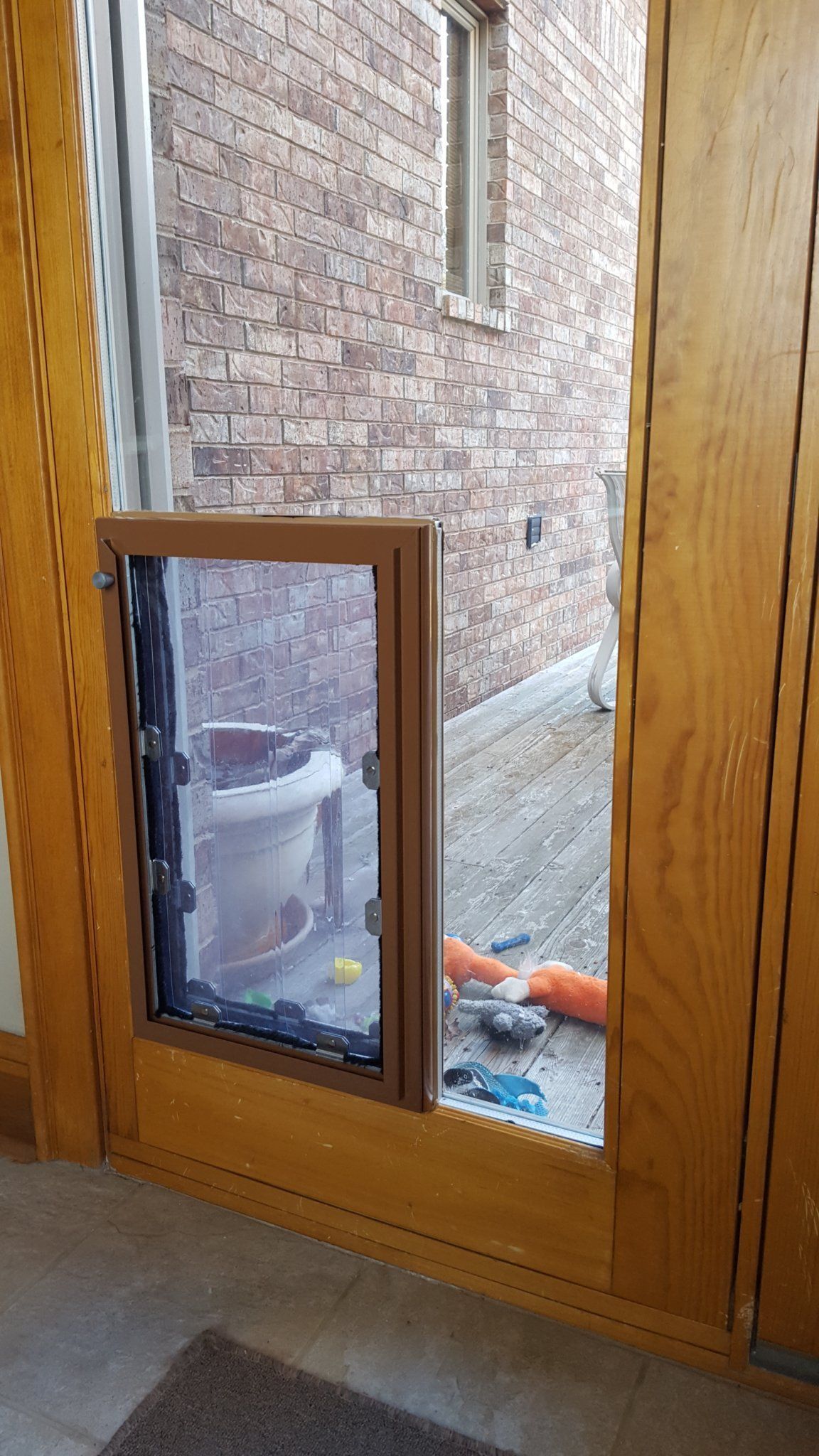 Wooden door with dog door installed, opening onto a deck with a brick wall.