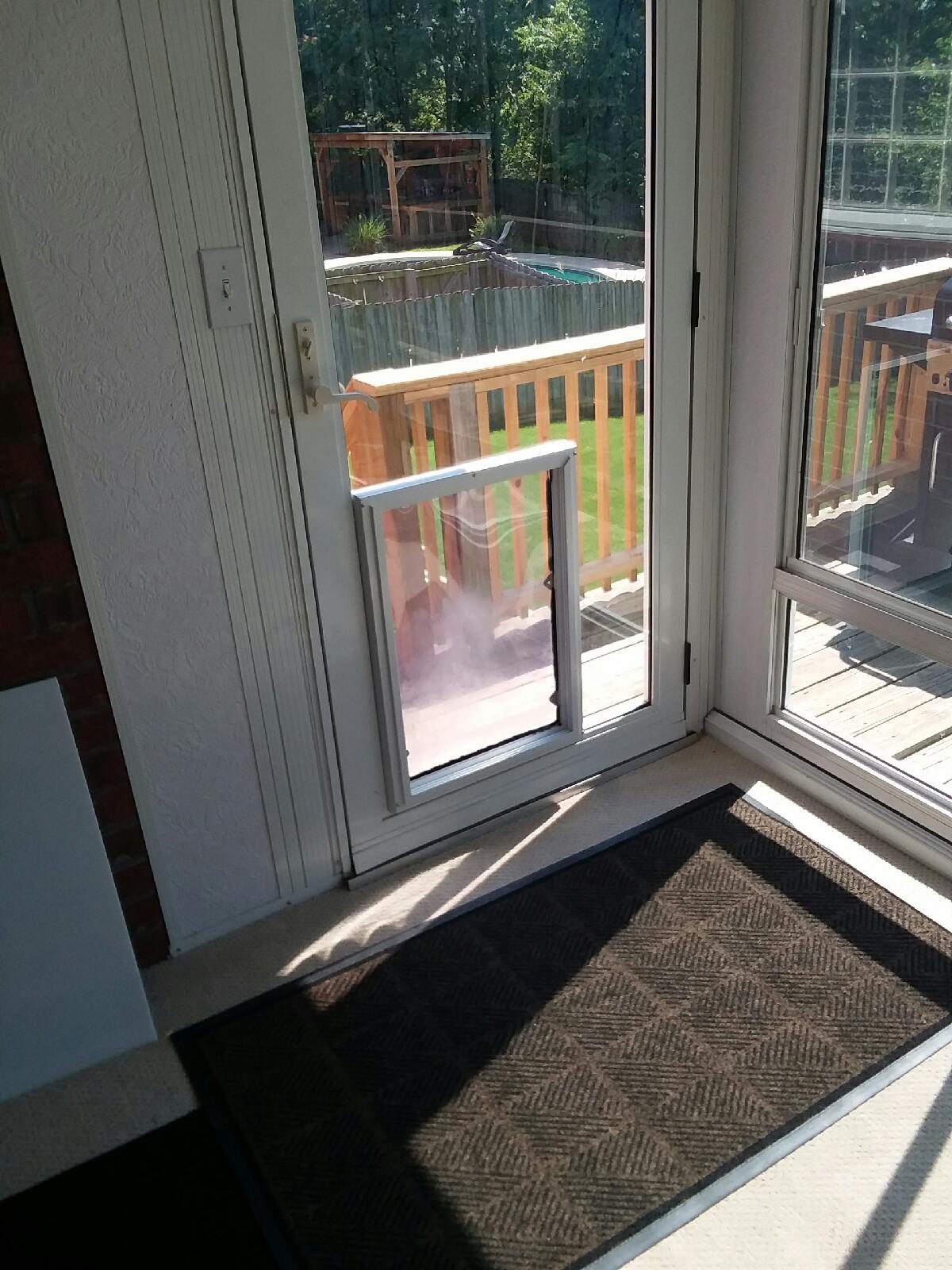 A white door with a dog door leads to a wooden deck and a pool.