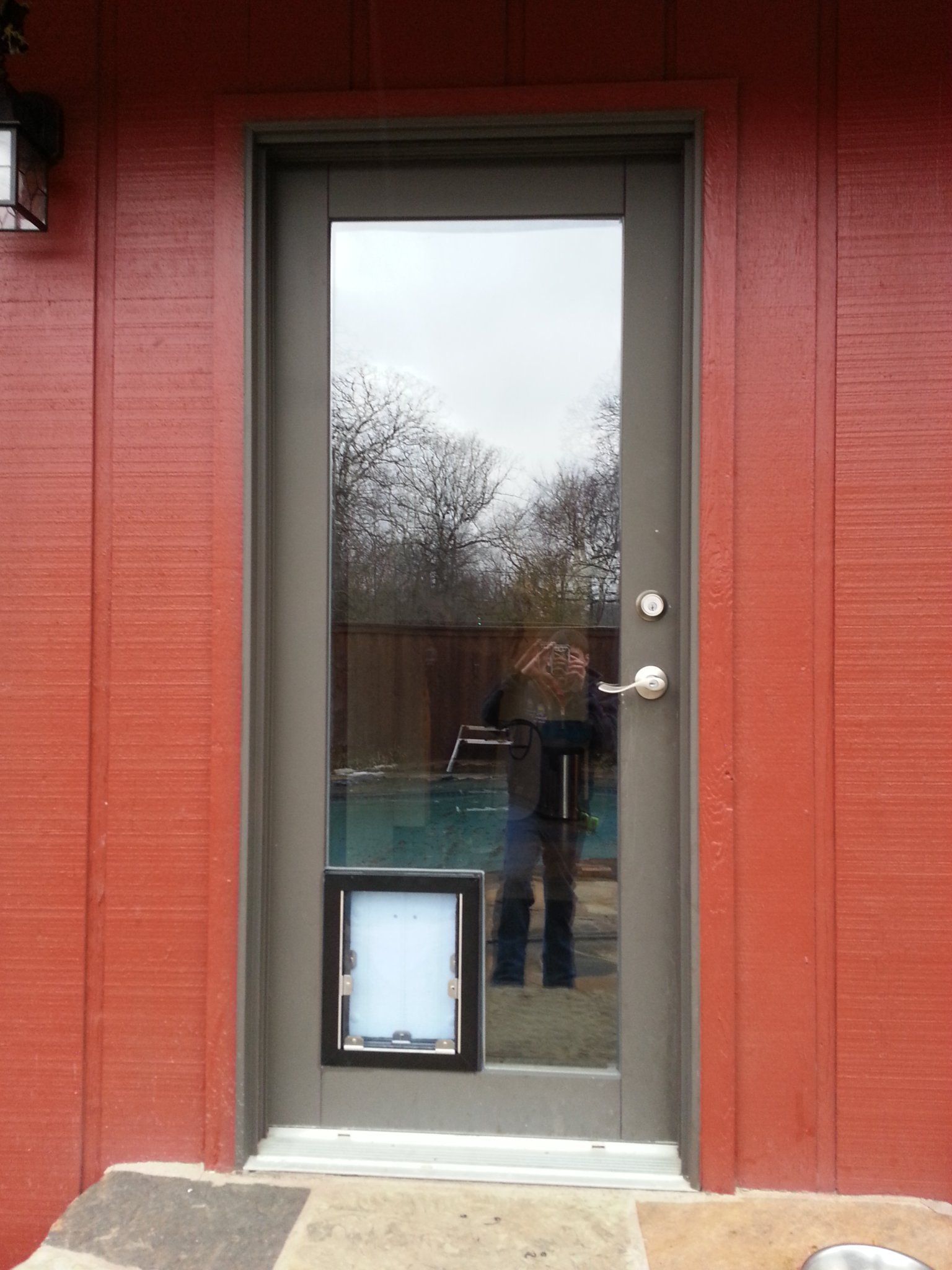 Dog door in a glass exterior door, set in a red-painted building exterior.