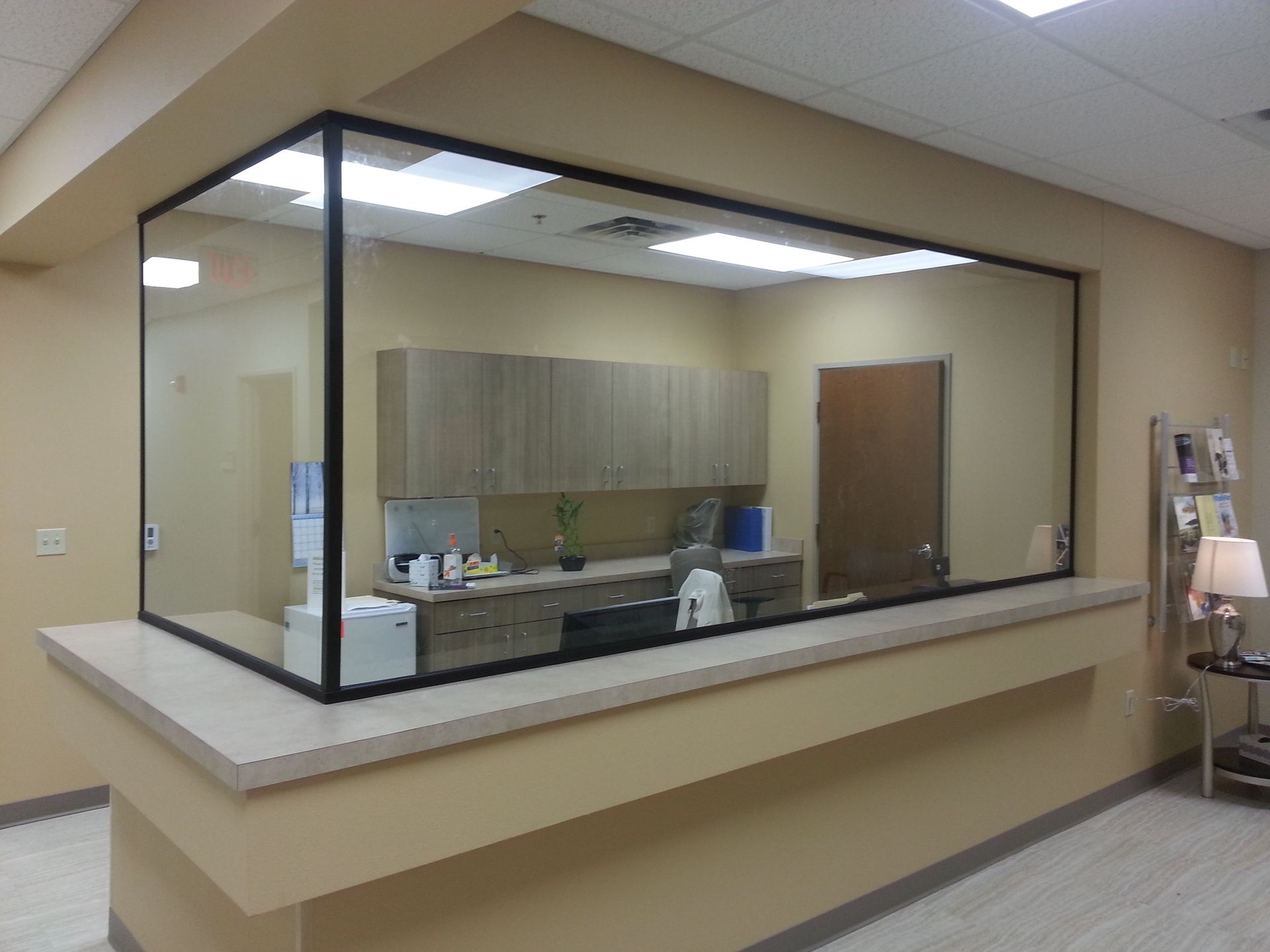 Reception desk with glass barrier, light beige walls, and cabinets visible inside.