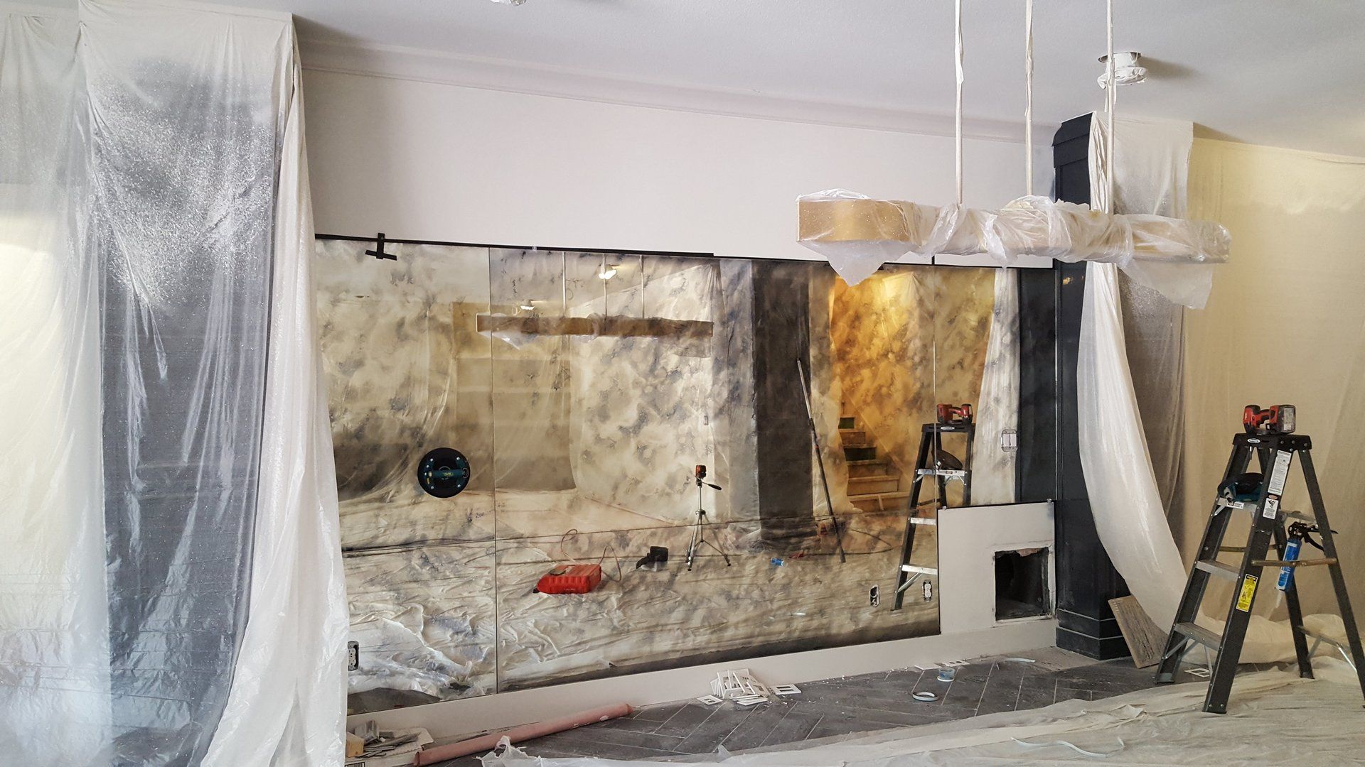 Renovation in progress: wall covered in plastic, ladder, exposed brick, and construction materials inside a room.
