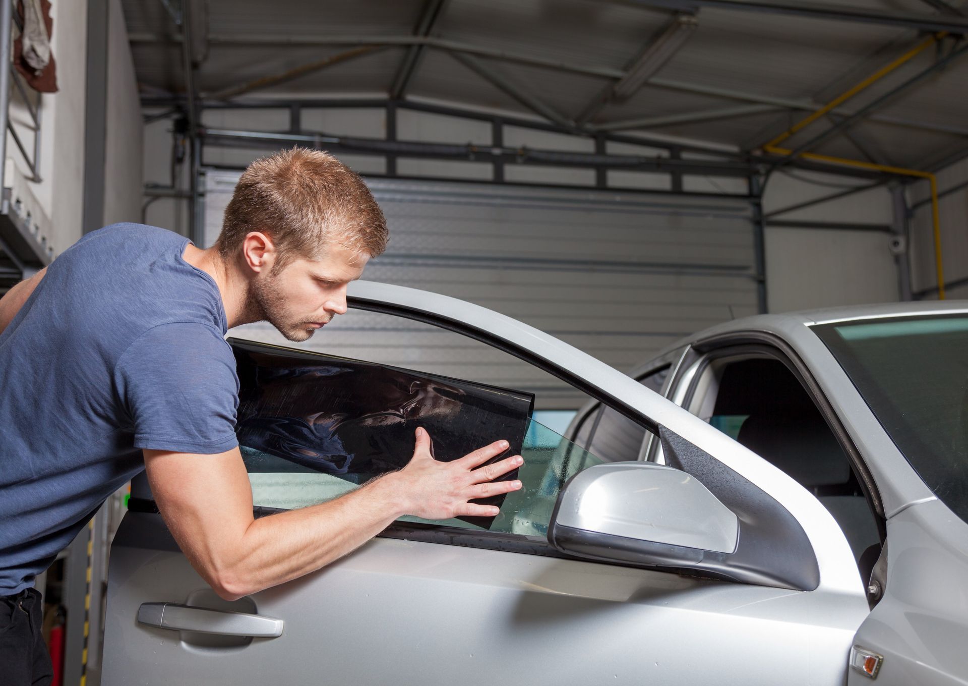 Man applying tint to a car window in a garage.