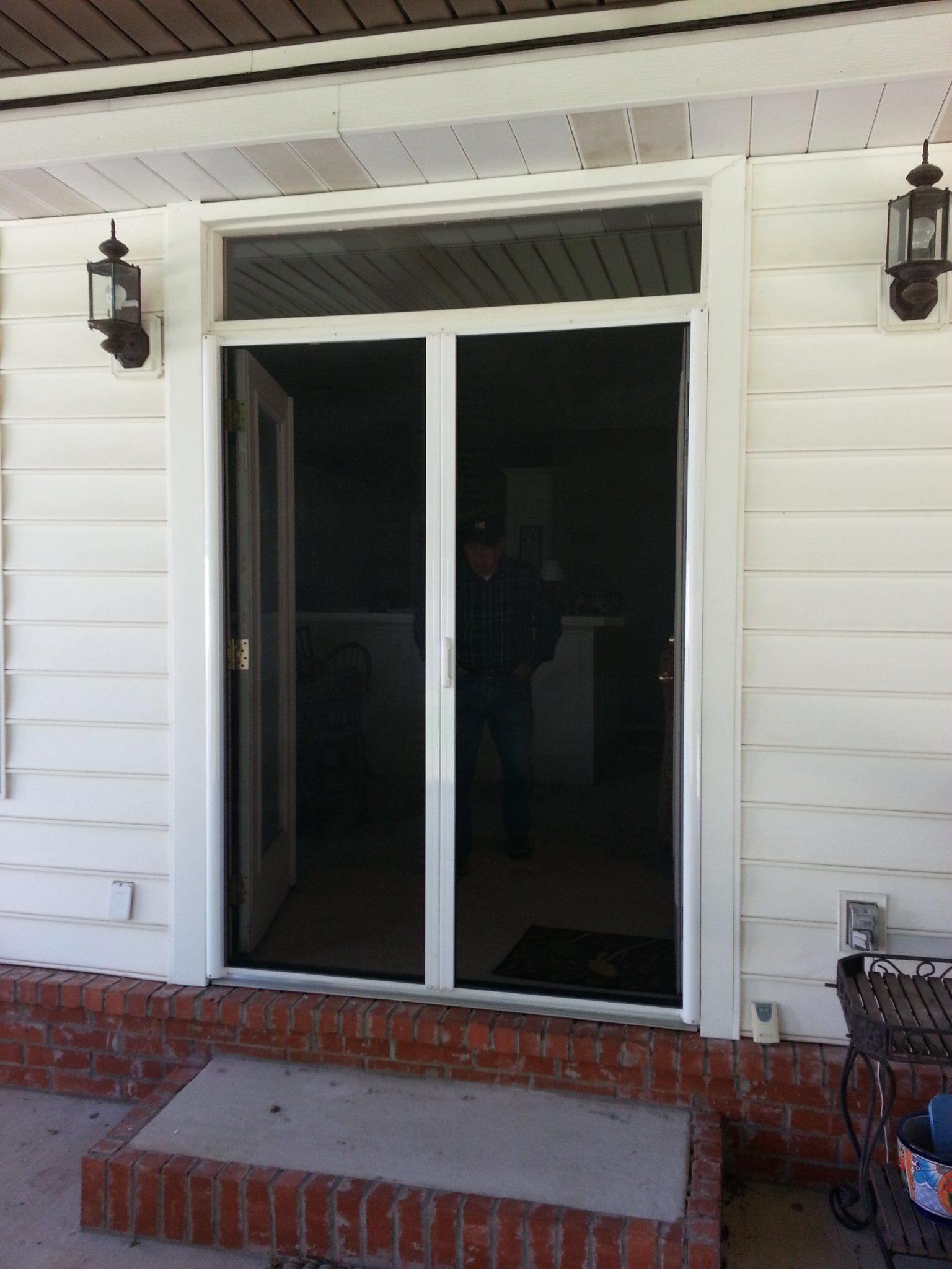 White screen door on a porch with a brick step and outdoor lights.