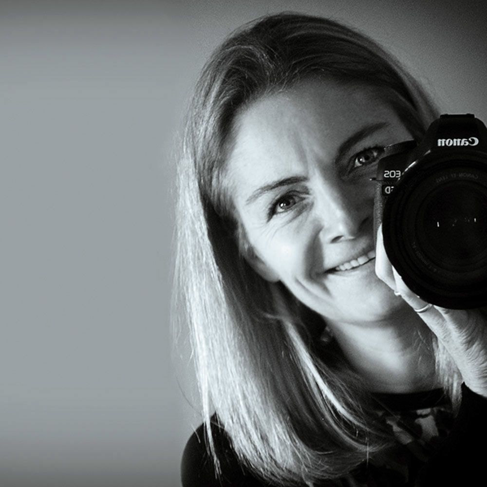 Ulrike Perkins holding a Canon camera up to her face as if she is taking a photo