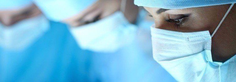 Surgeon wearing a mask and cap, focused in a bright operating room.