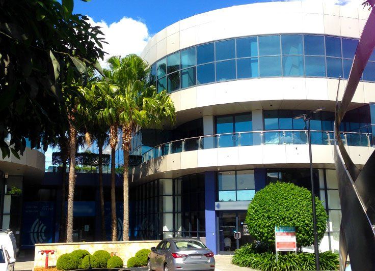 Modern, multi-story building with blue-tinted windows, palm trees, and a parked car.