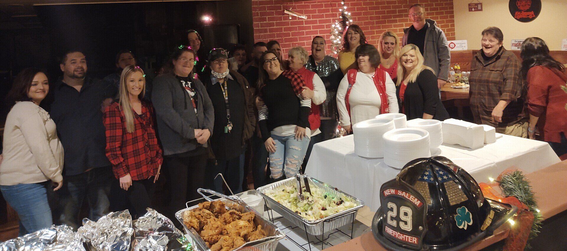 A group of people at a gathering with food, a firefighter's helmet, and Christmas decorations.