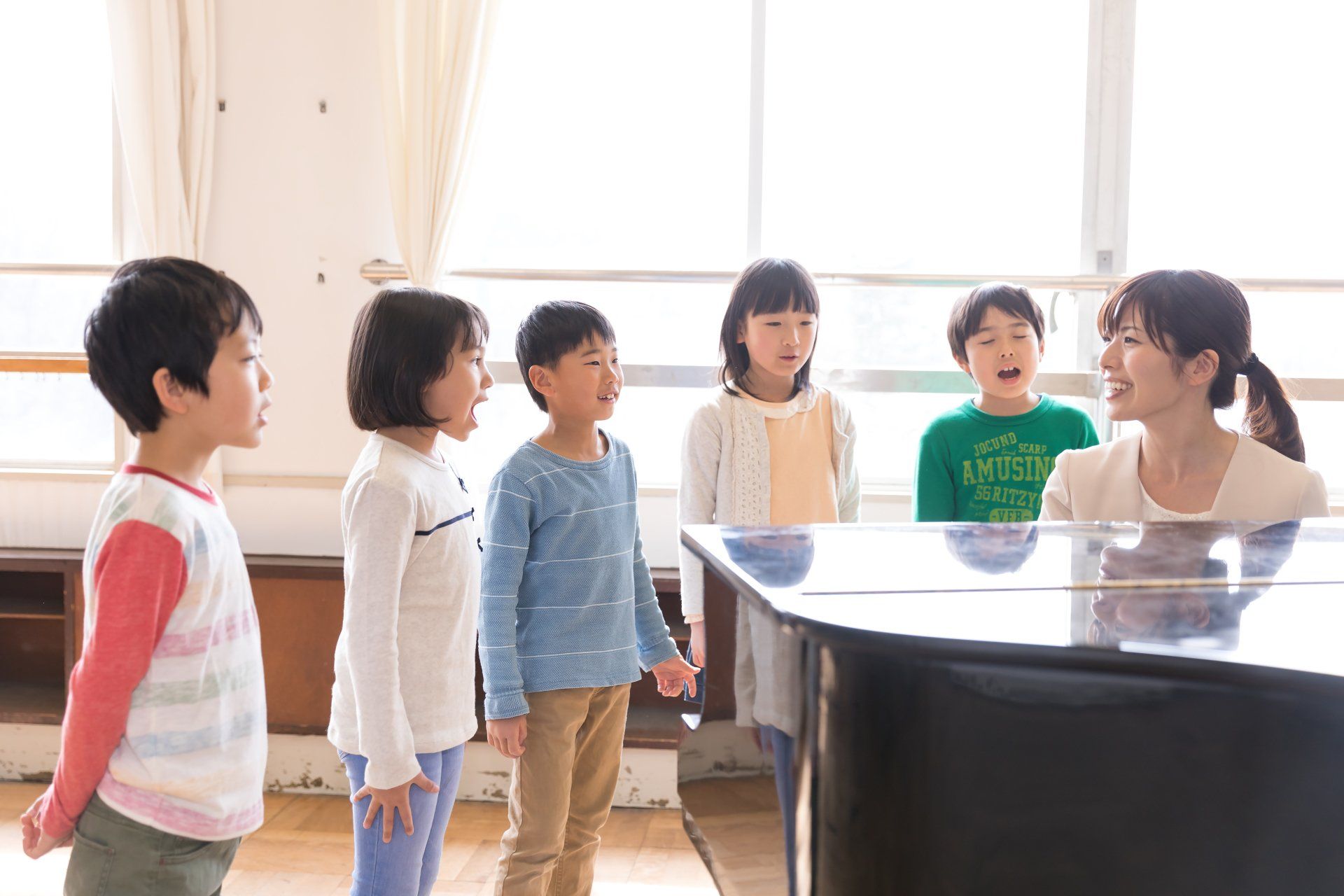 孩子們站在明亮的音樂教室裡,圍著鋼琴,看著彈琴的人。