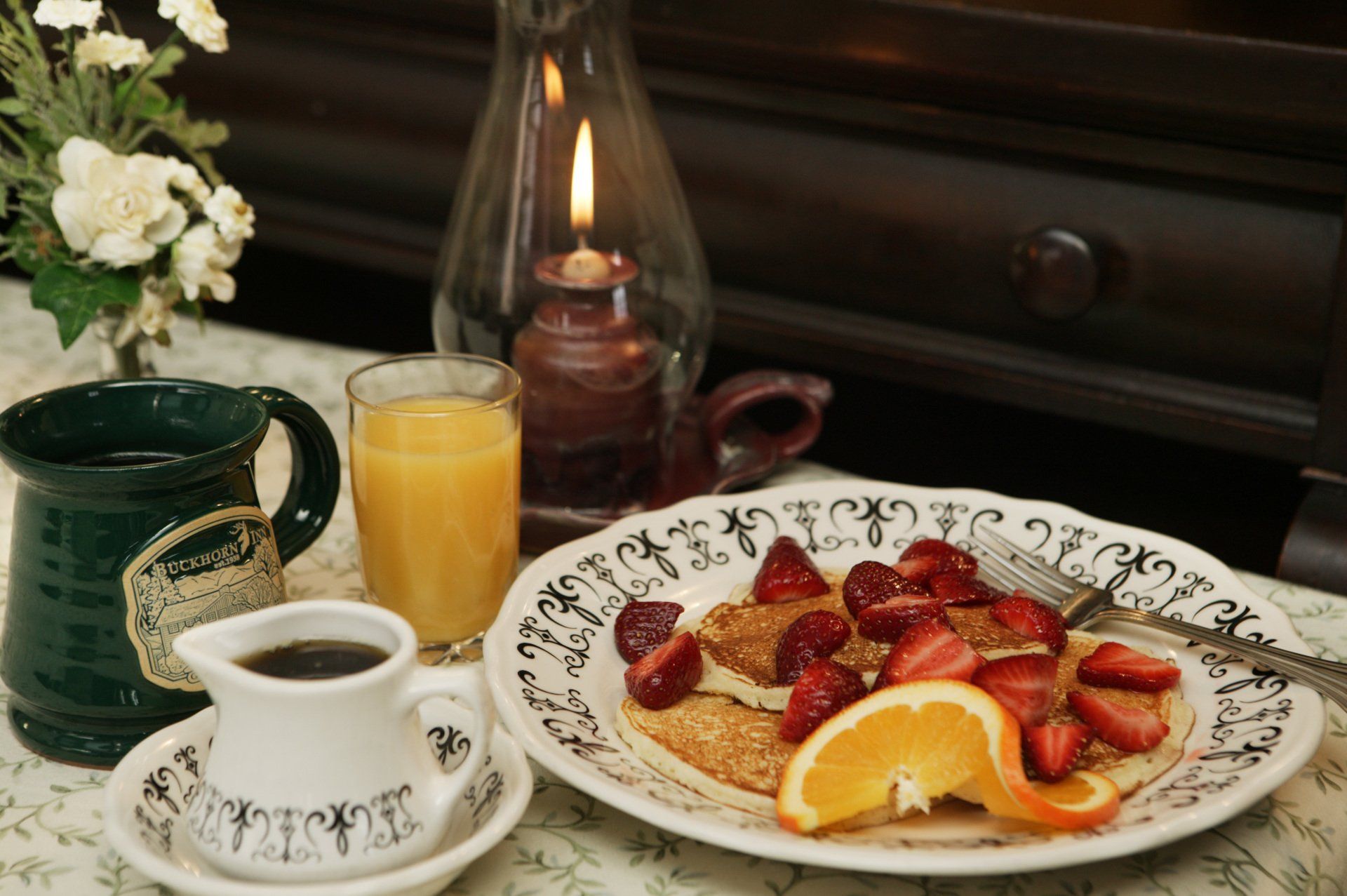 A plate of pancakes with strawberries and oranges next to a cup of coffee