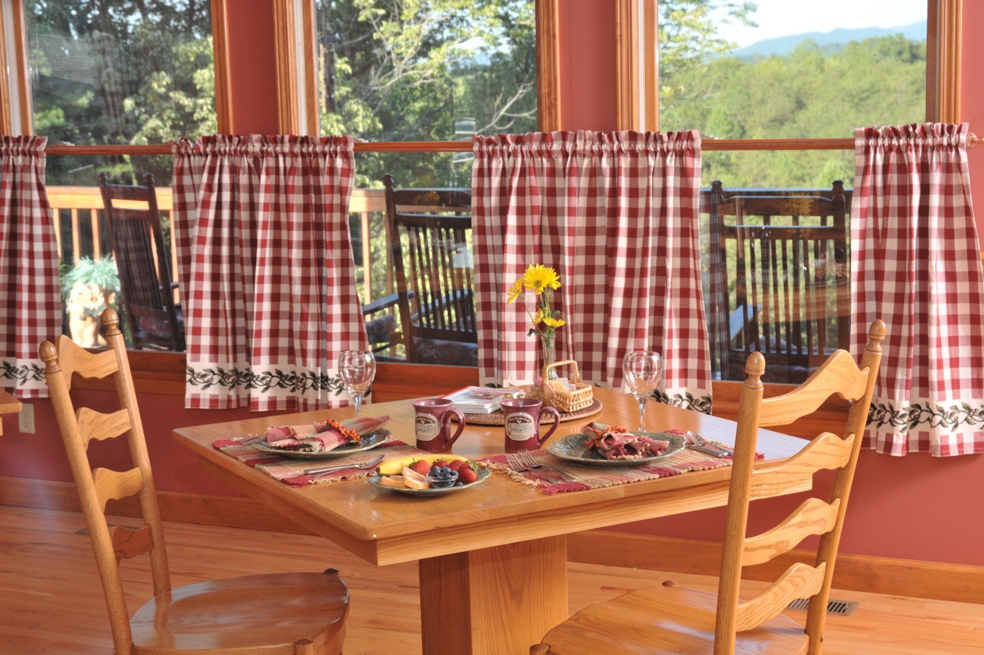 A dining room table with plates of food on it and red and white checkered curtains.
