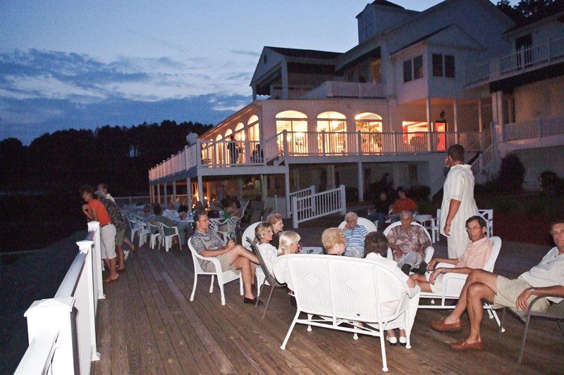 A group of people are sitting on a deck in front of a large house