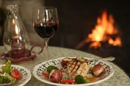 A plate of food and a glass of wine are on a table in front of a fireplace.